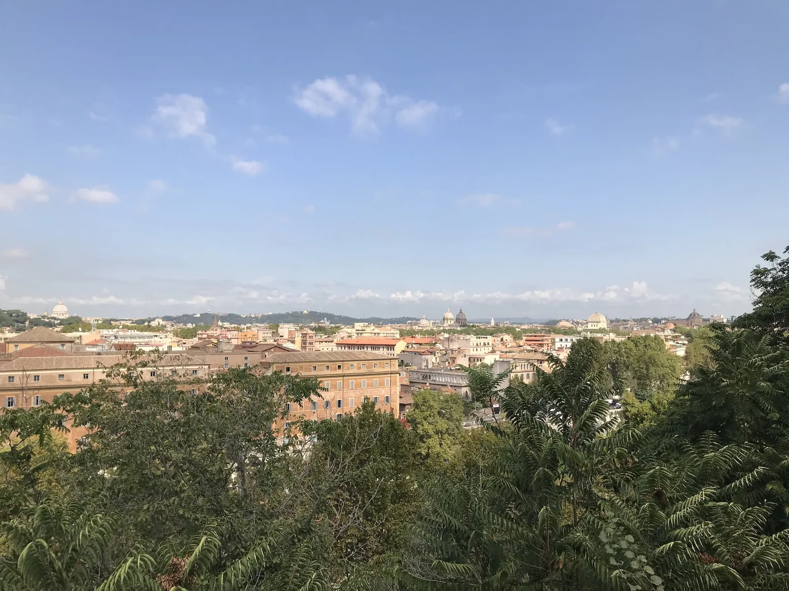 Wide view of Rome's rooftops from the Aventine belvedere with St Peter's dome in the distance.