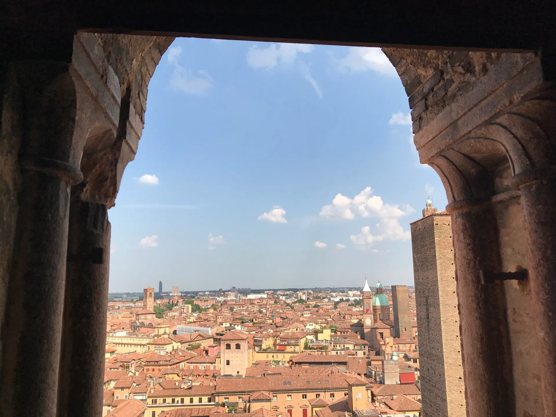 Bologna rooftops and a medieval tower framed by a stone arch opening in the bell tower.