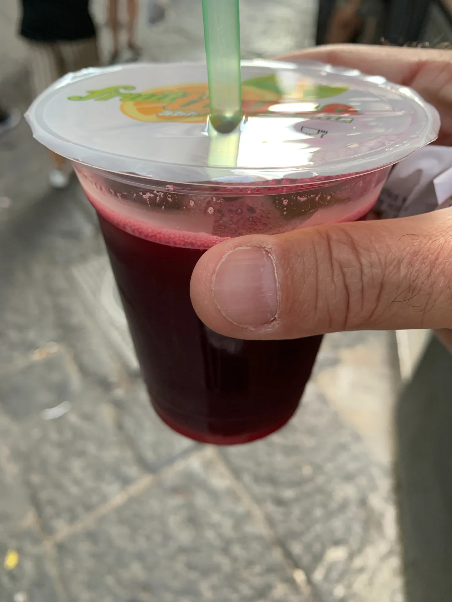 A cold fruit drink held in hand on a street in Naples