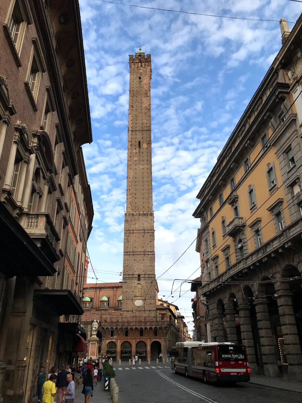 Looking straight up the brick shaft of the Asinelli tower against a cloudy sky.