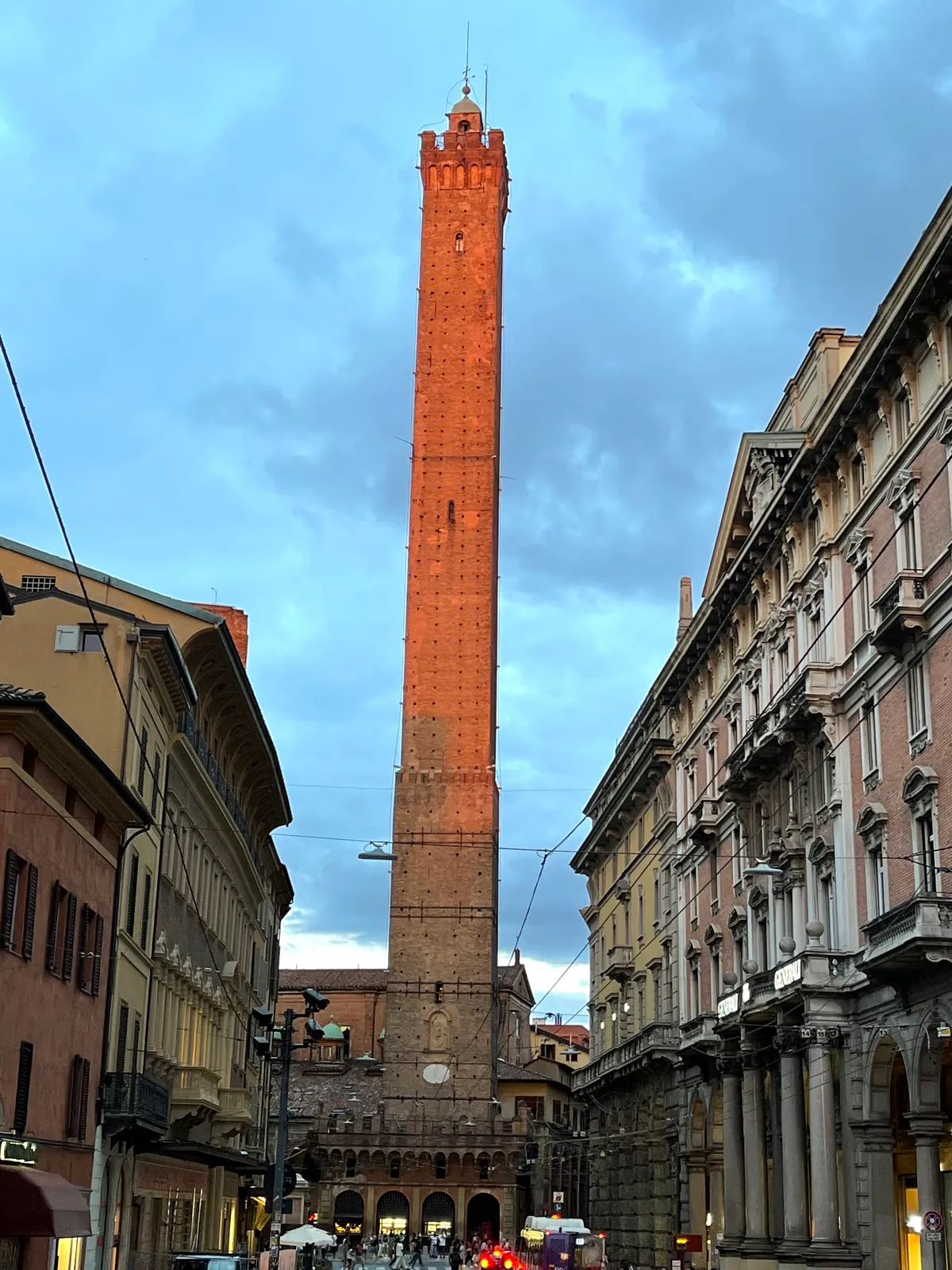 The Asinelli tower glowing orange in low evening sun above Via Rizzoli.