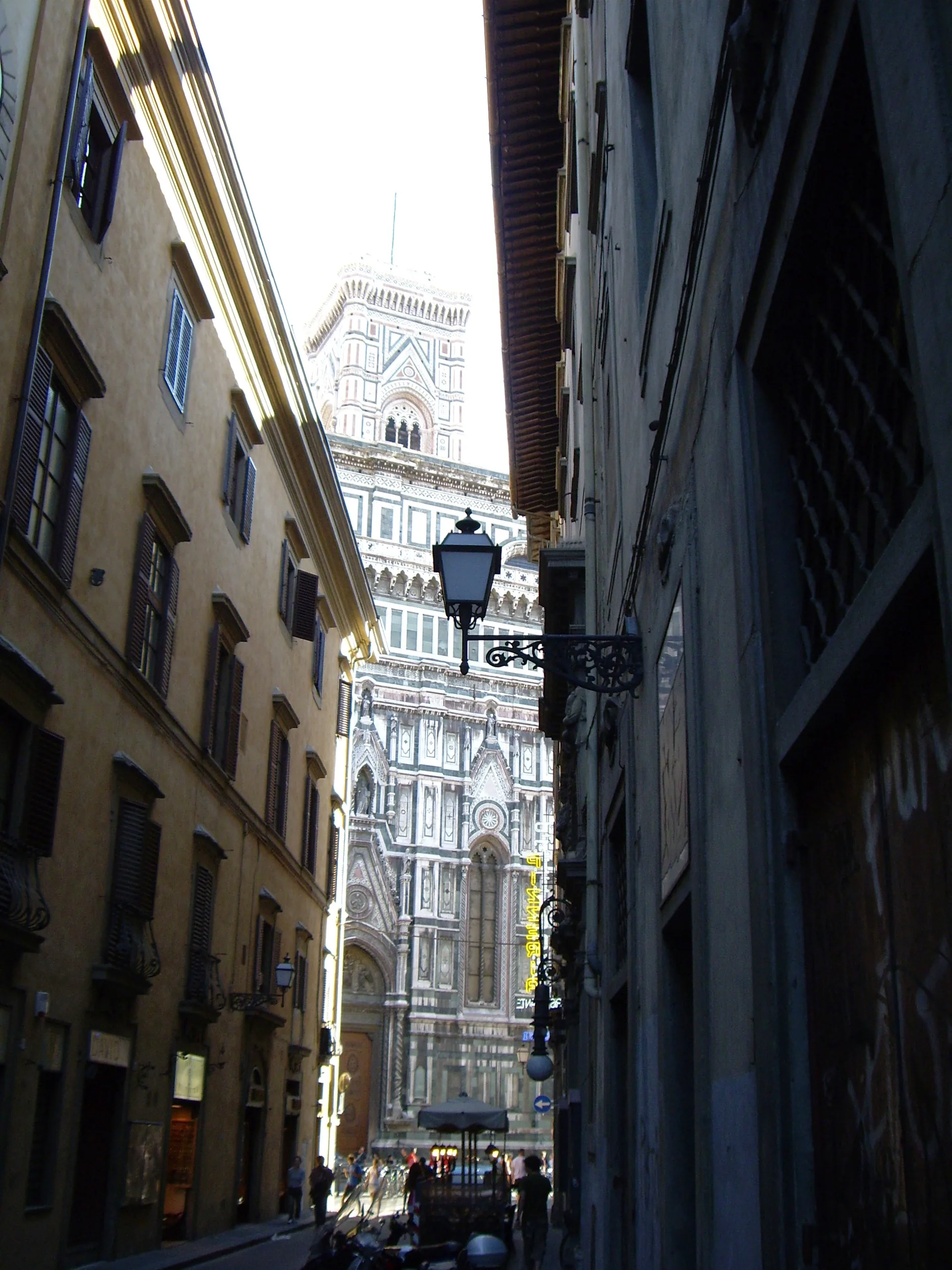 The marble flank of the cathedral appearing at the end of a narrow Florentine street