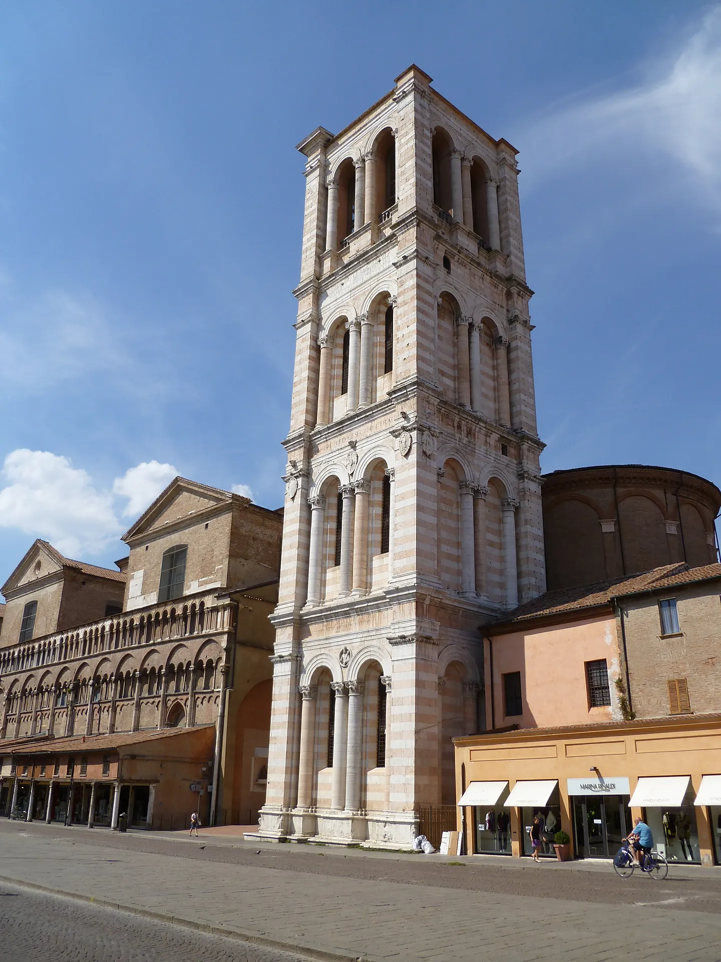 The white and pink marble Renaissance bell tower of Ferrara Cathedral against a blue sky.