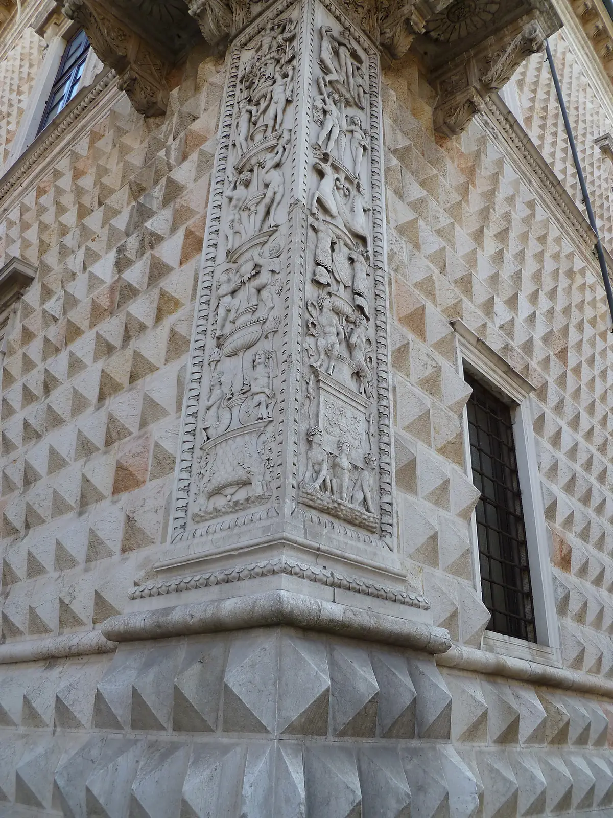 Close view of the carved marble candelabra pilaster at the corner of Palazzo dei Diamanti, set against diamond-cut blocks.