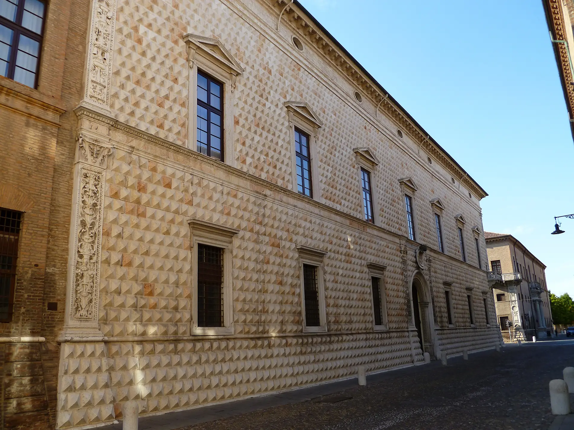 The long diamond-rusticated marble facade of Palazzo dei Diamanti in Ferrara receding down a street.