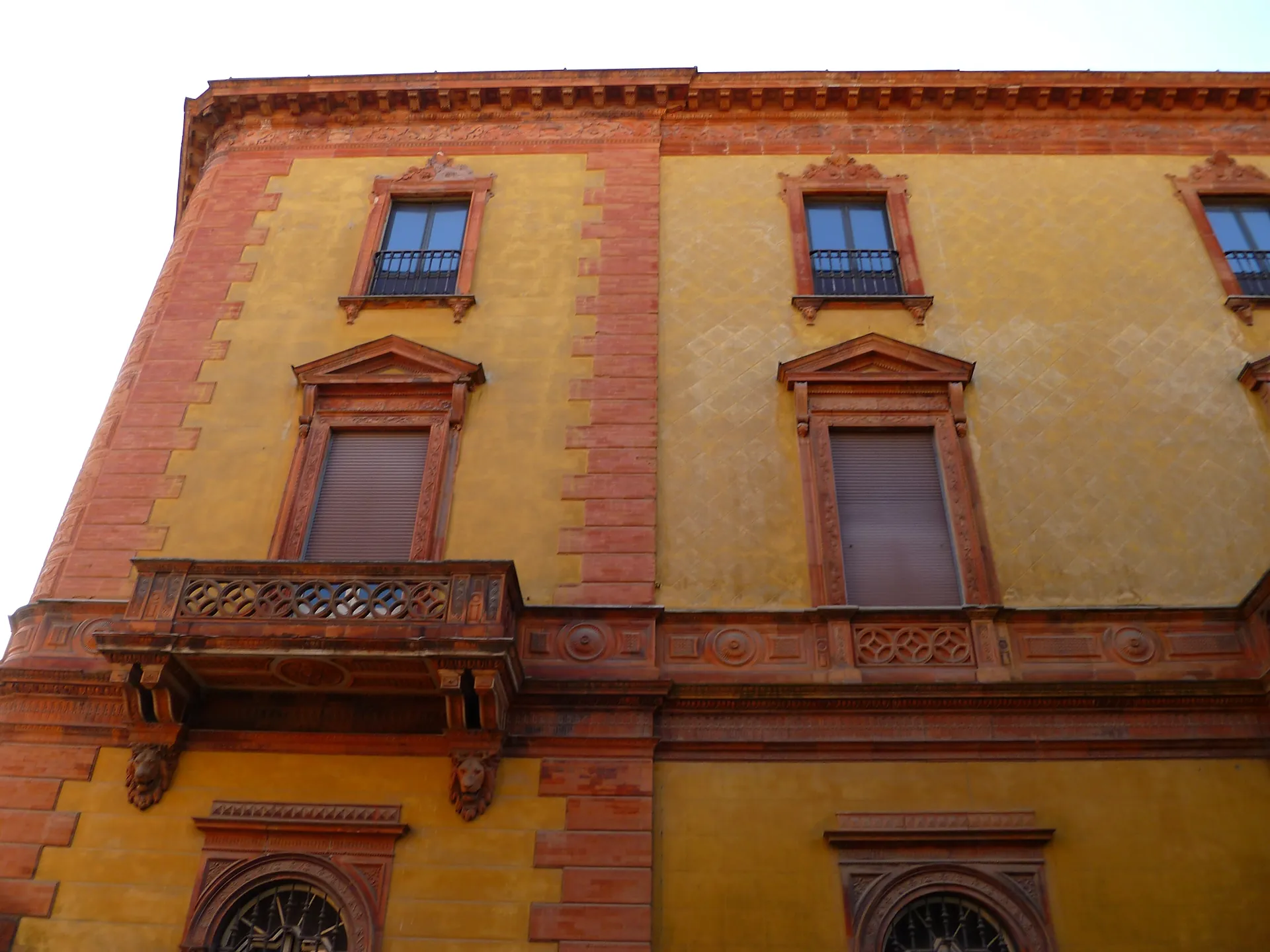 A yellow corner palazzo in Ferrara with a white marble balcony and tall arched windows.