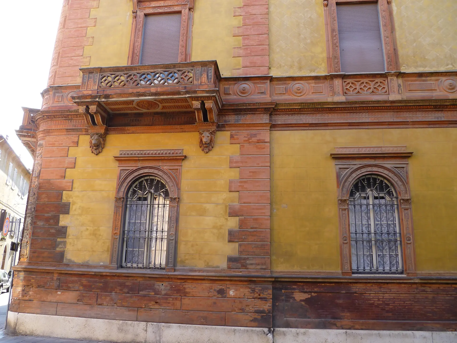 An ochre-yellow Ferrara palazzo facade with a carved stone balcony and arched windows.