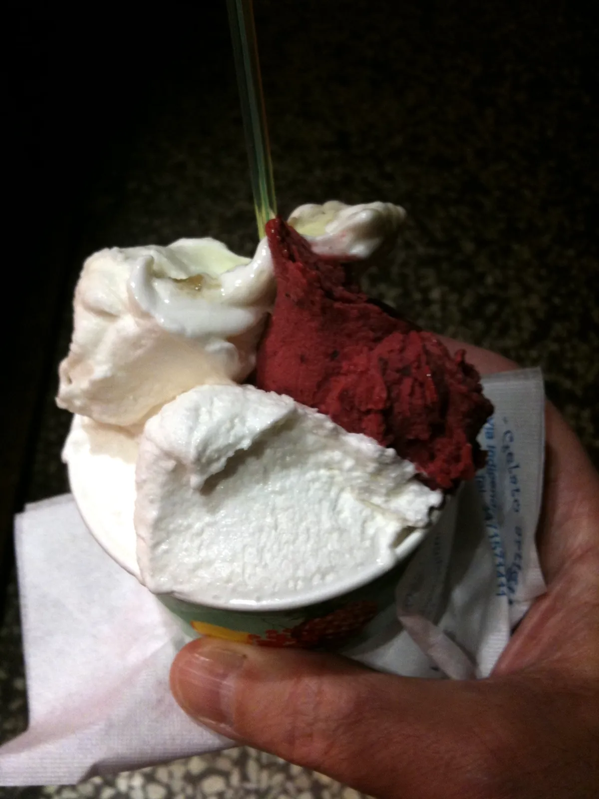 A paper cup of gelato with a fruit sorbet scoop beside a cream scoop.
