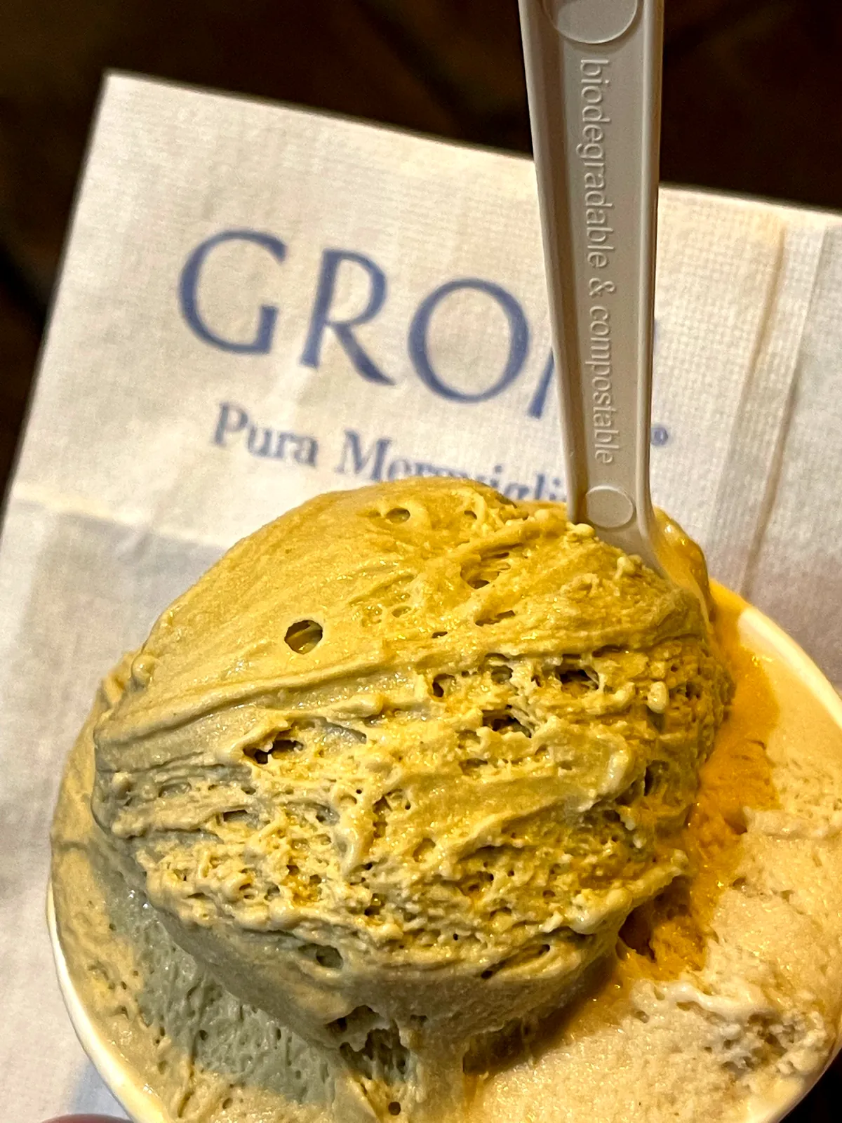 A scoop of muted green pistachio gelato in a paper cup from Grom.