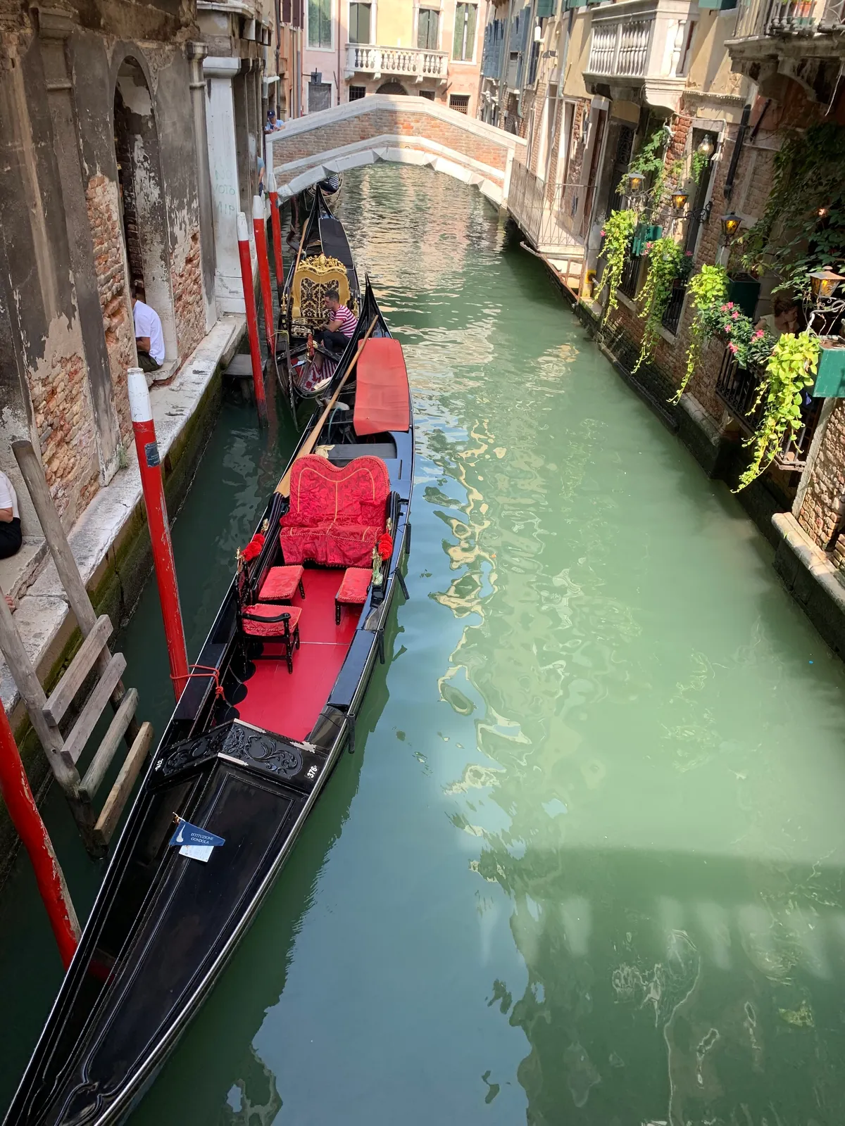 A gondola with red seats moored on a narrow green Venetian canal