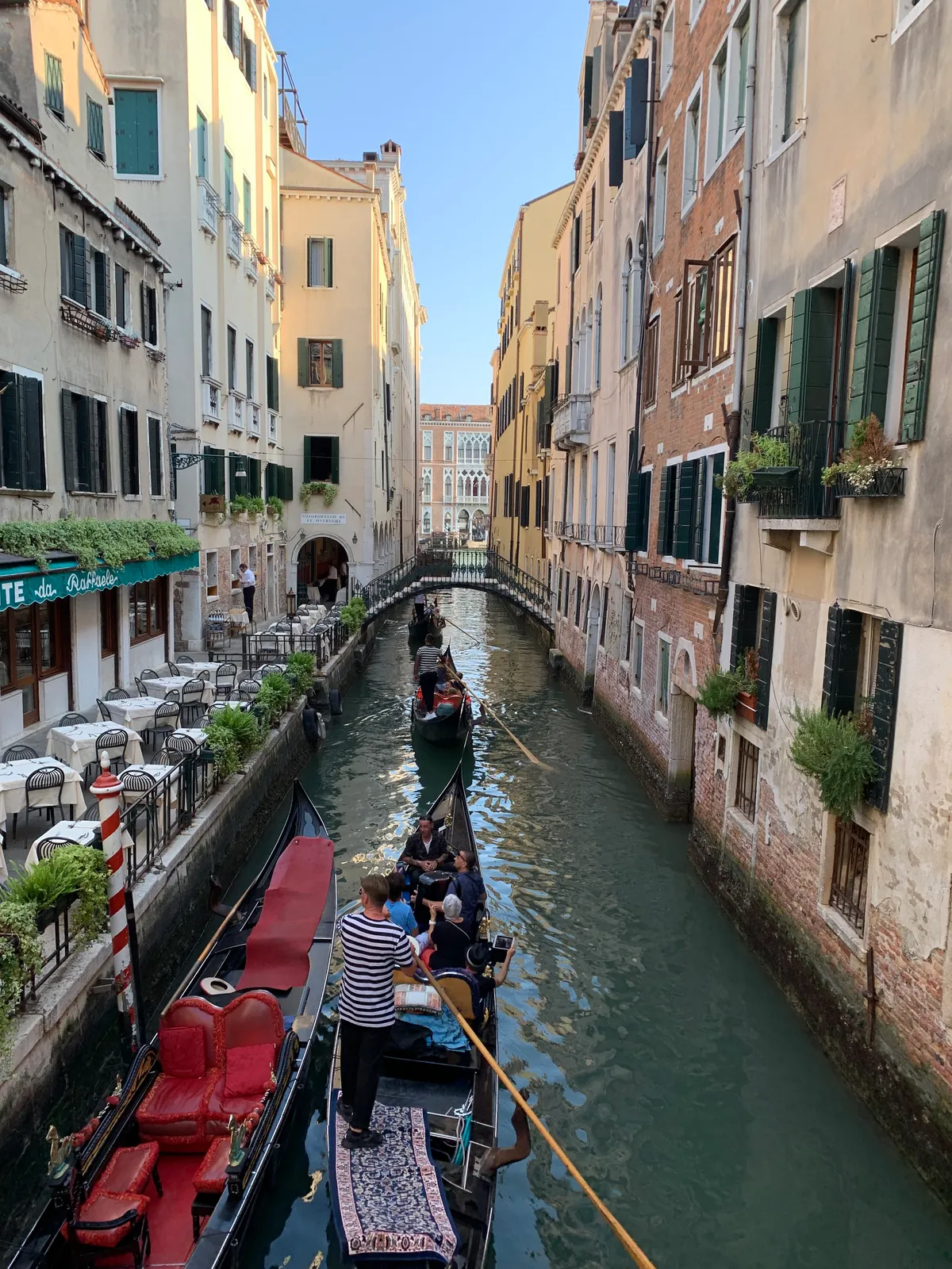 The view down a narrow Venetian canal from a gondola, with other gondolas ahead