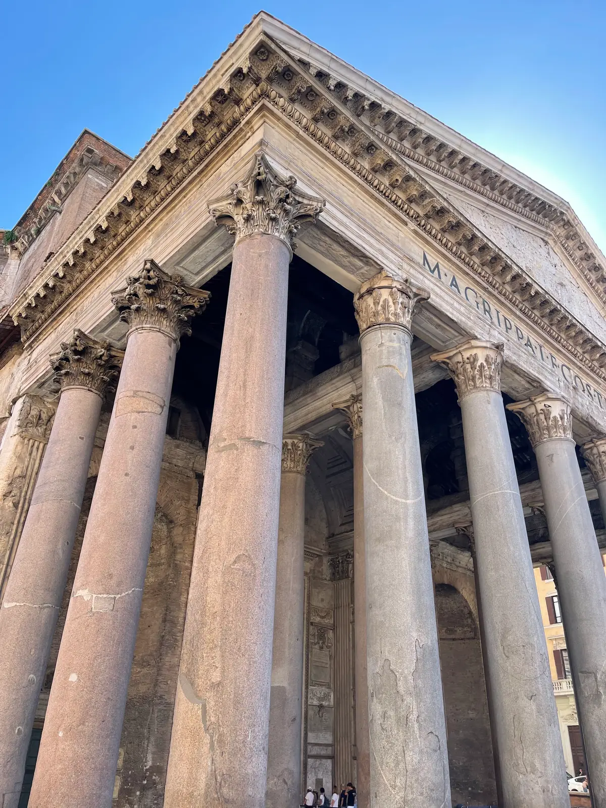 Looking up at the Pantheon portico granite columns and Corinthian capitals against a blue sky