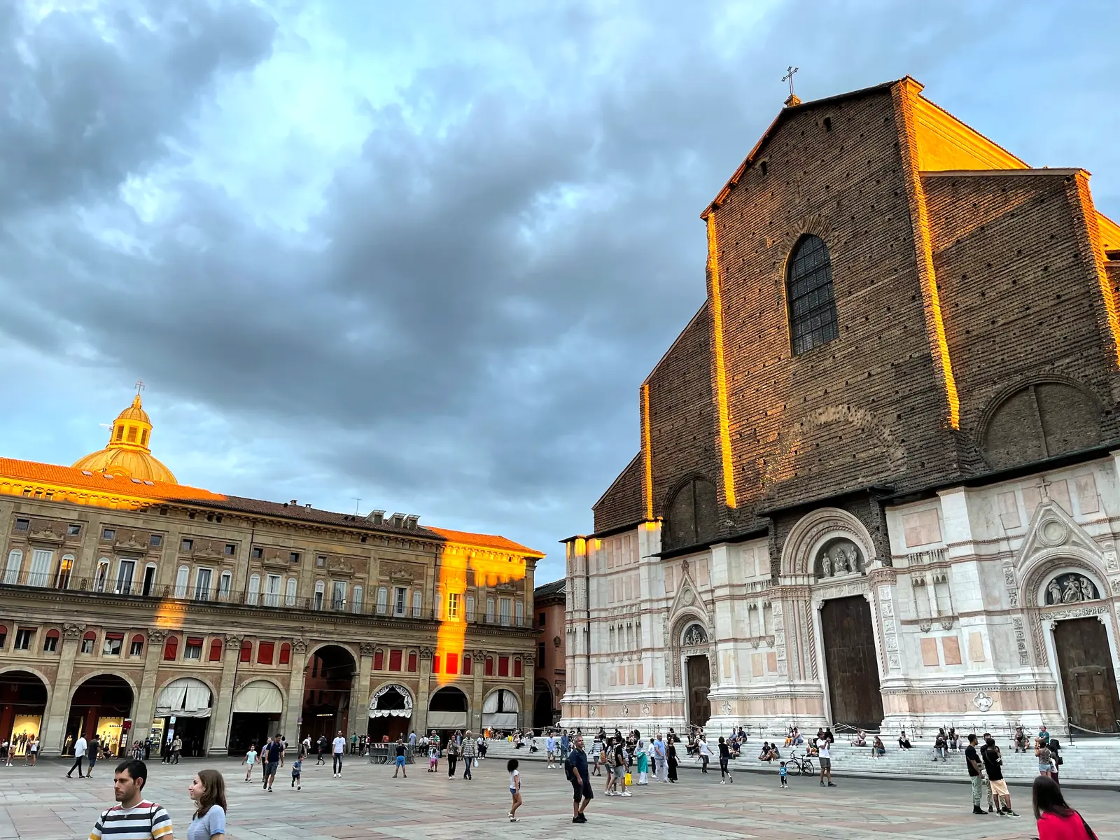 The brick side of San Petronio glowing orange at sunset under dark clouds.