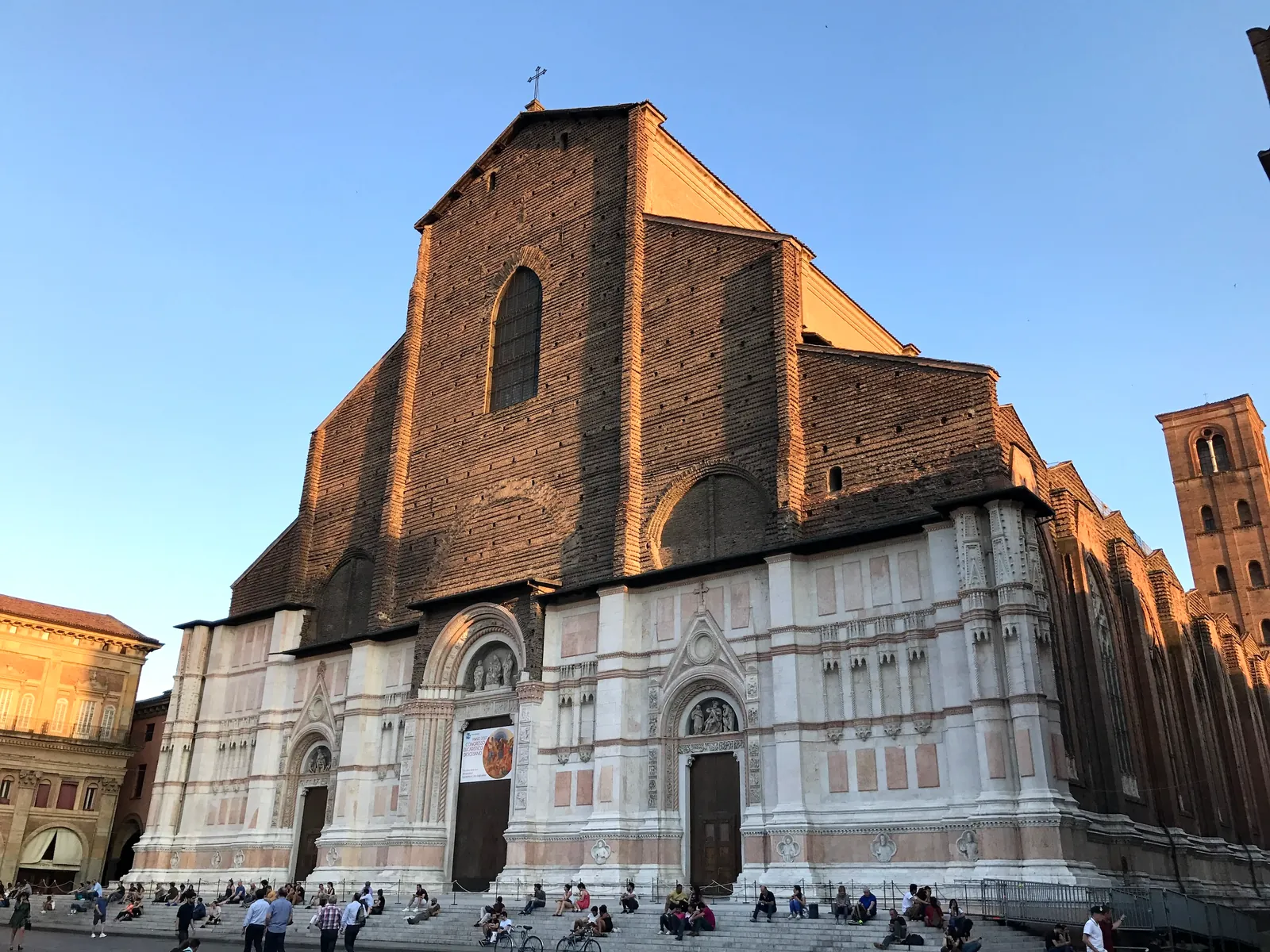 The facade of San Petronio in warm late light with people on the steps.