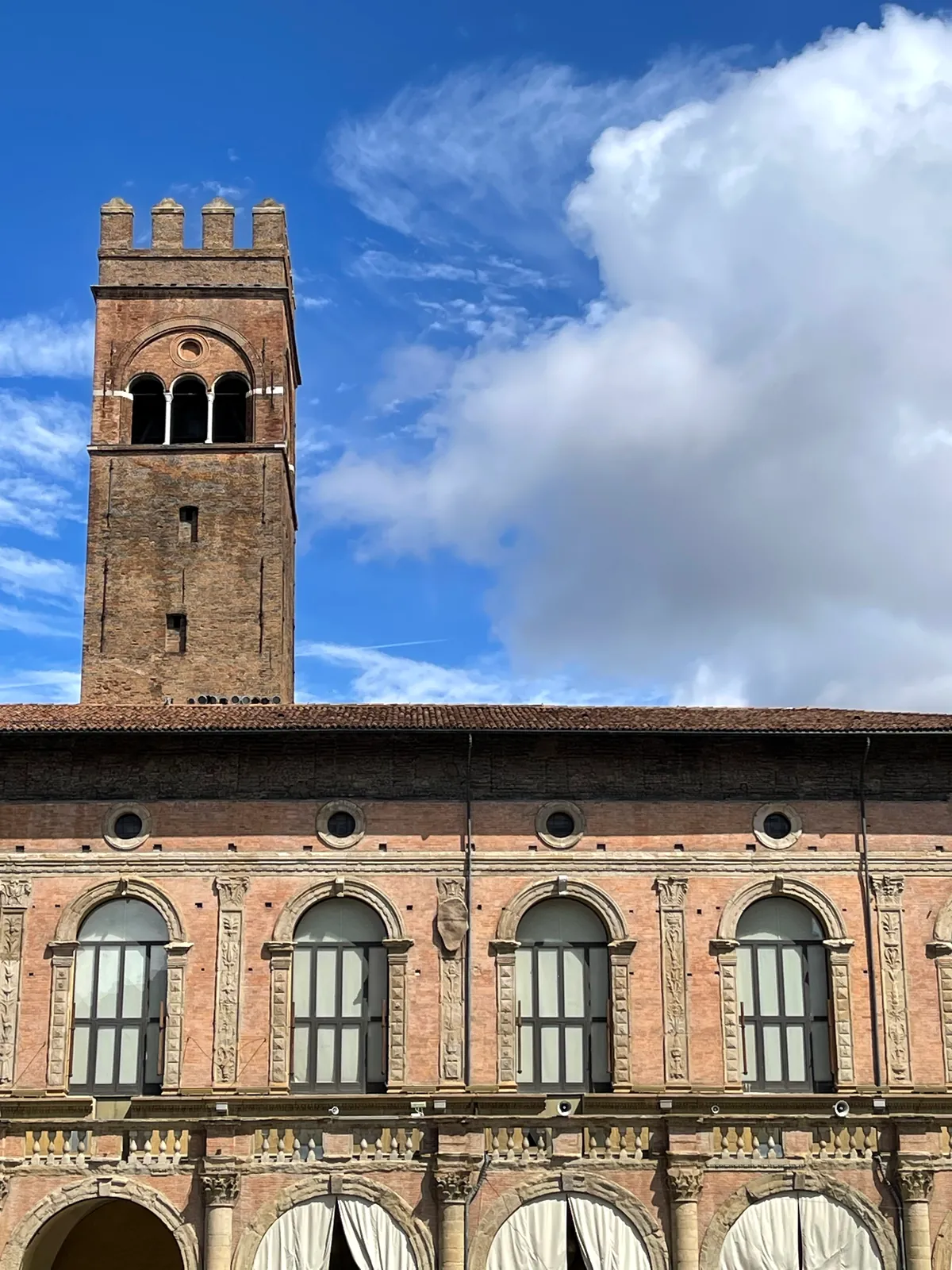 The brick tower and loggia of Palazzo Re Enzo under a blue sky.