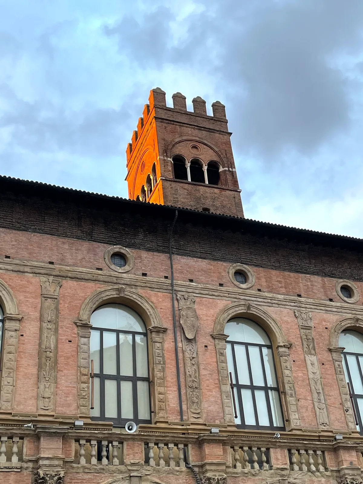 Piazza Maggiore at dusk with the lit clock tower of Palazzo d'Accursio.