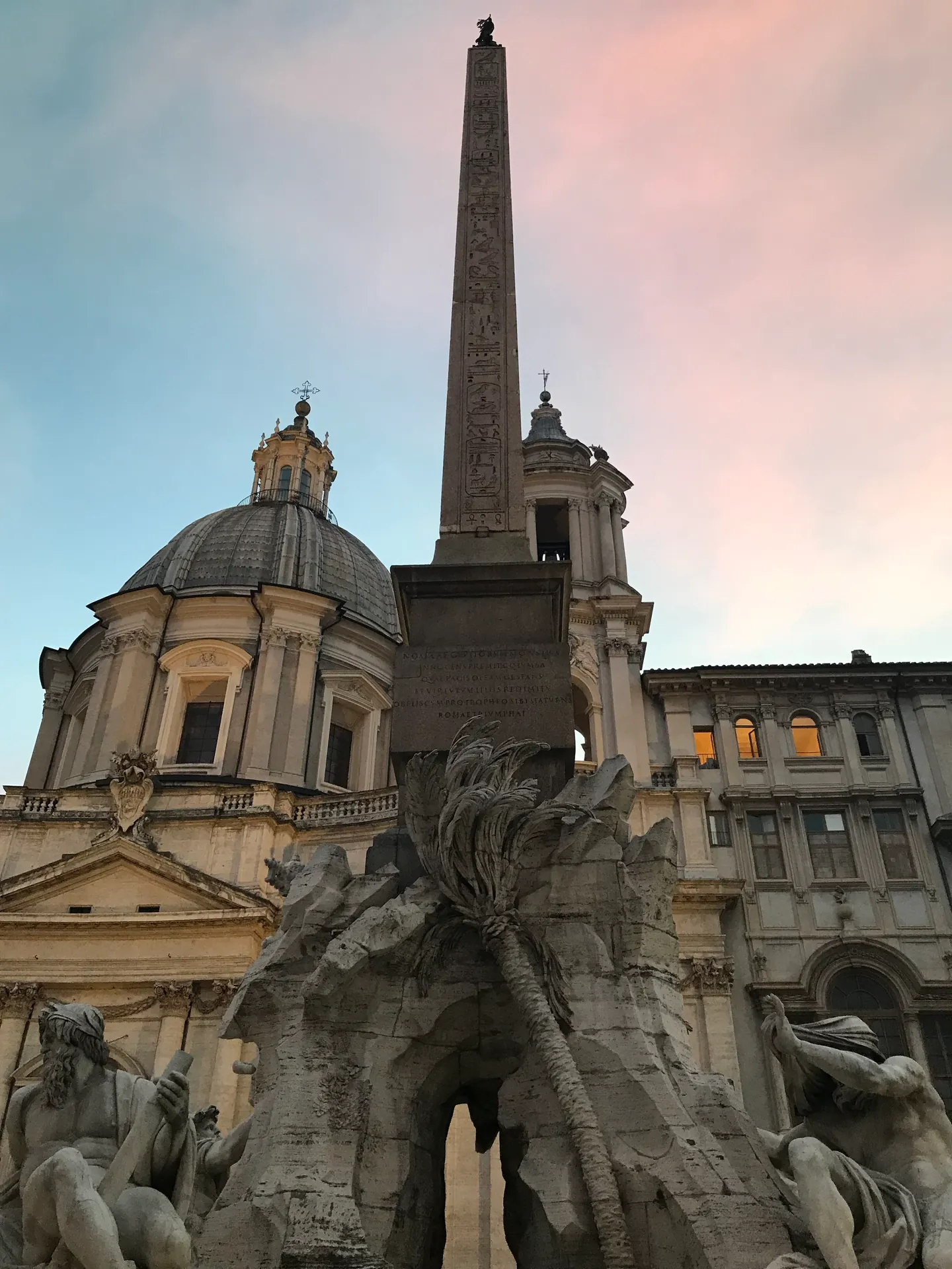 Obelisk and dome of Sant'Agnese in Agone against a pink dusk sky at Piazza Navona