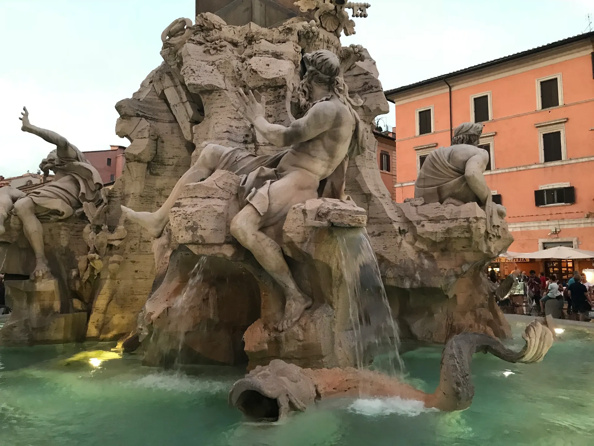 Water cascading from the Four Rivers fountain at dusk with lit basin water