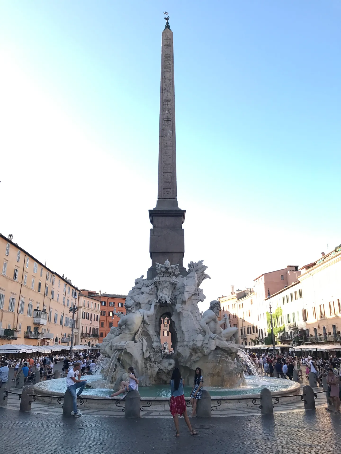 Four Rivers fountain and obelisk at golden hour with visitors seated on the rim