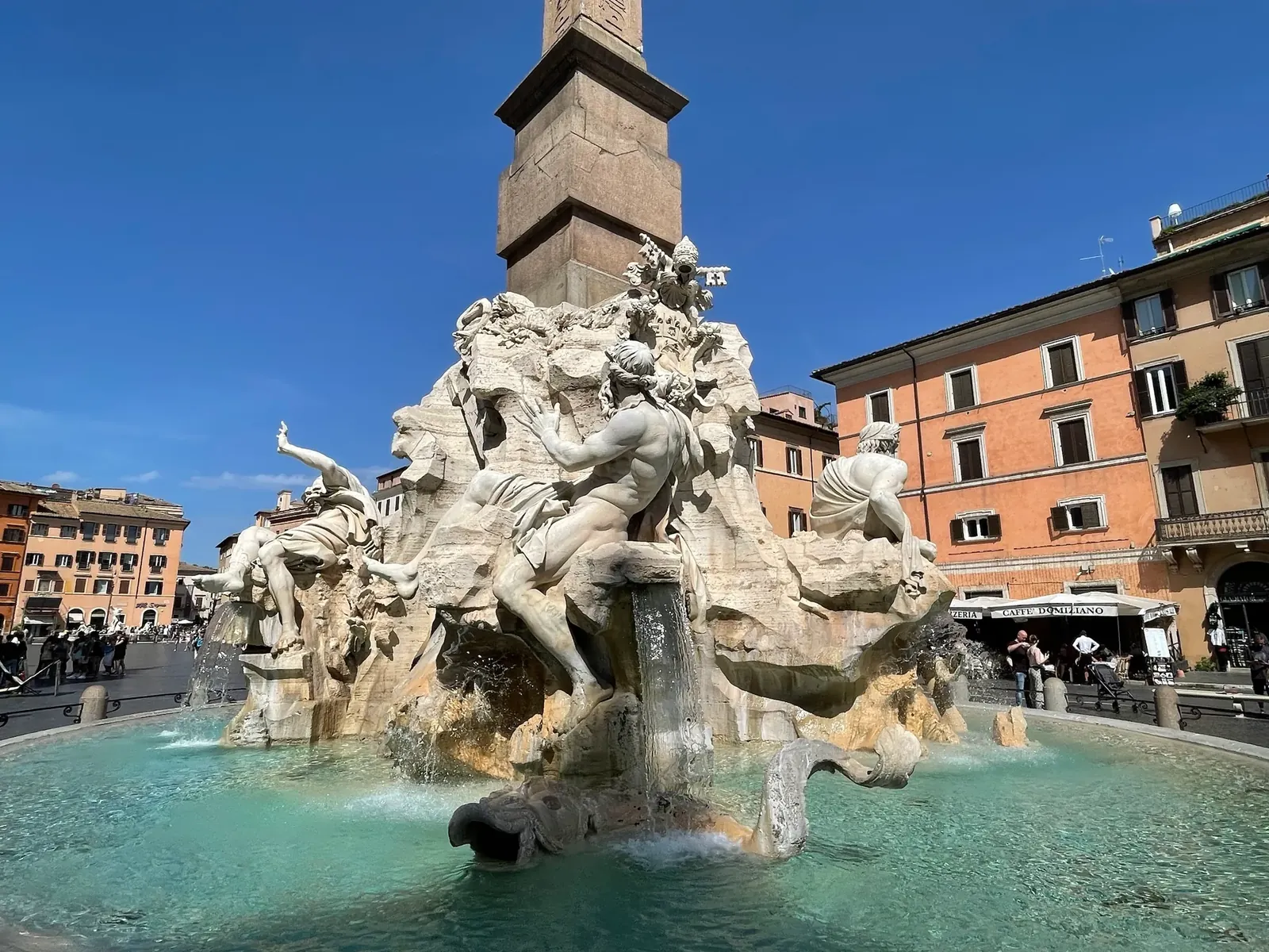 West face of the Four Rivers fountain in bright sun with turquoise water in the basin