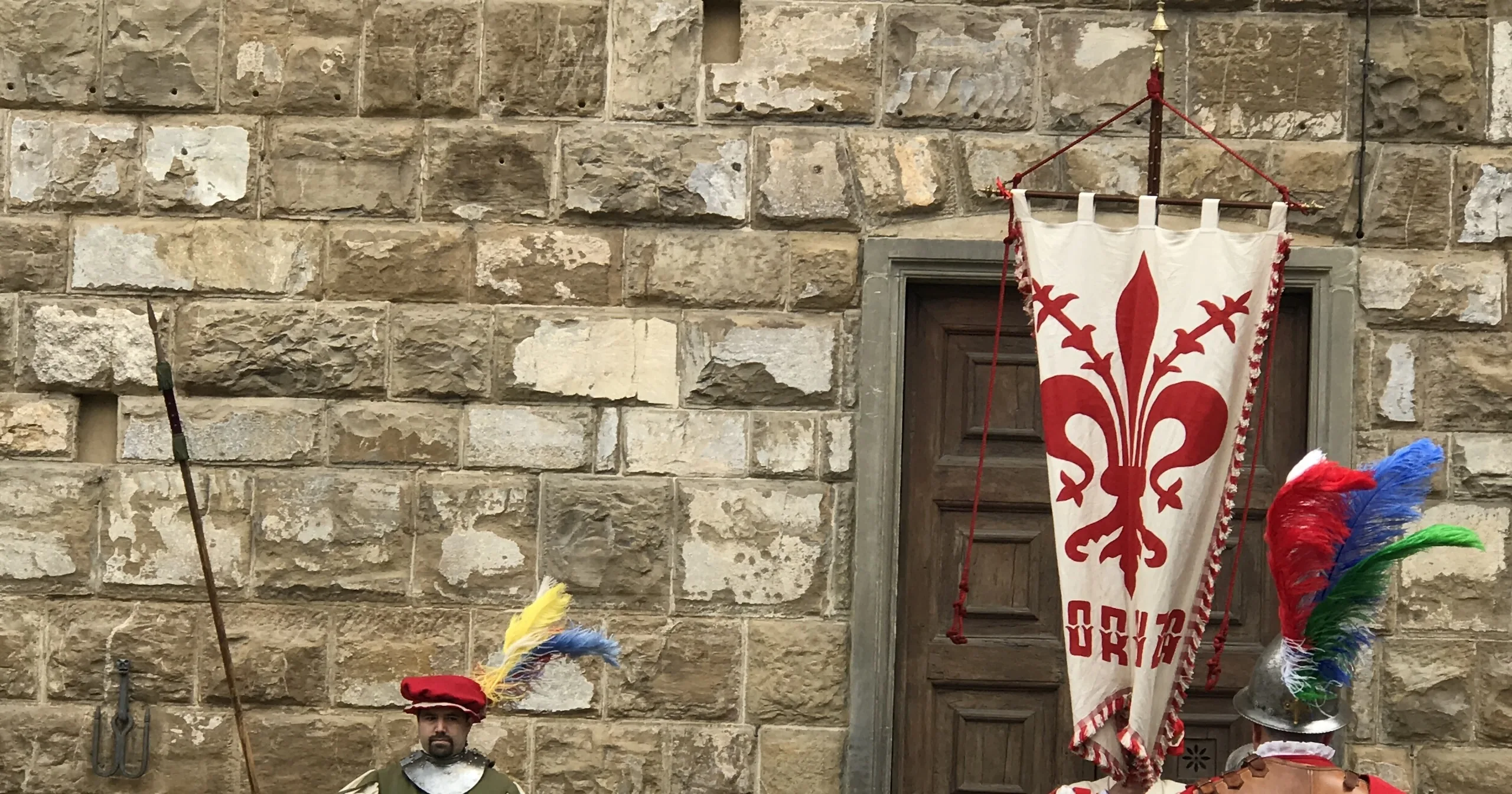 The lily banner of Florence and plumed helmets of costumed guards against the stone of the Palazzo Vecchio