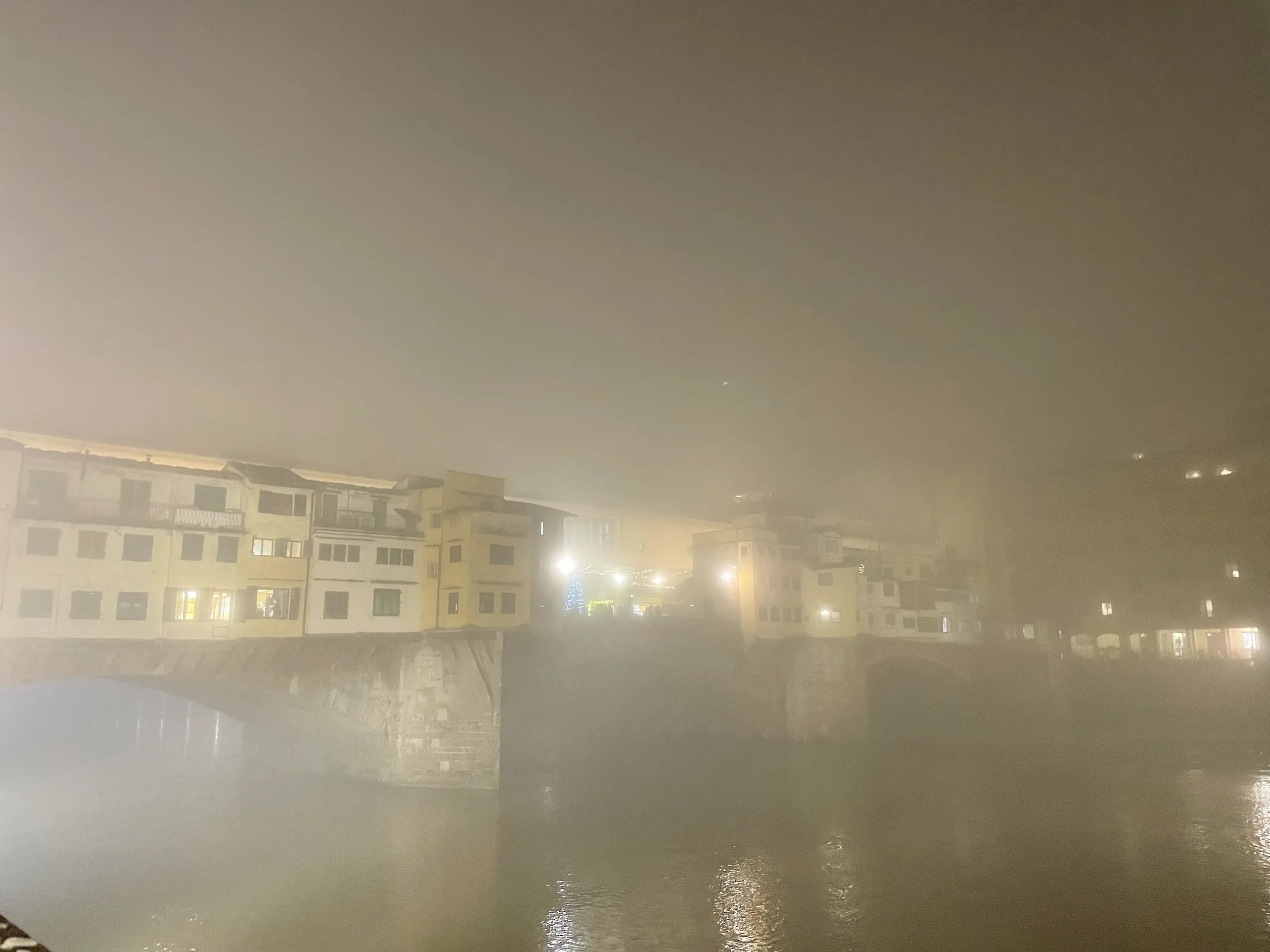 The Ponte Vecchio nearly lost in dense winter fog, only its lamps and lit windows showing