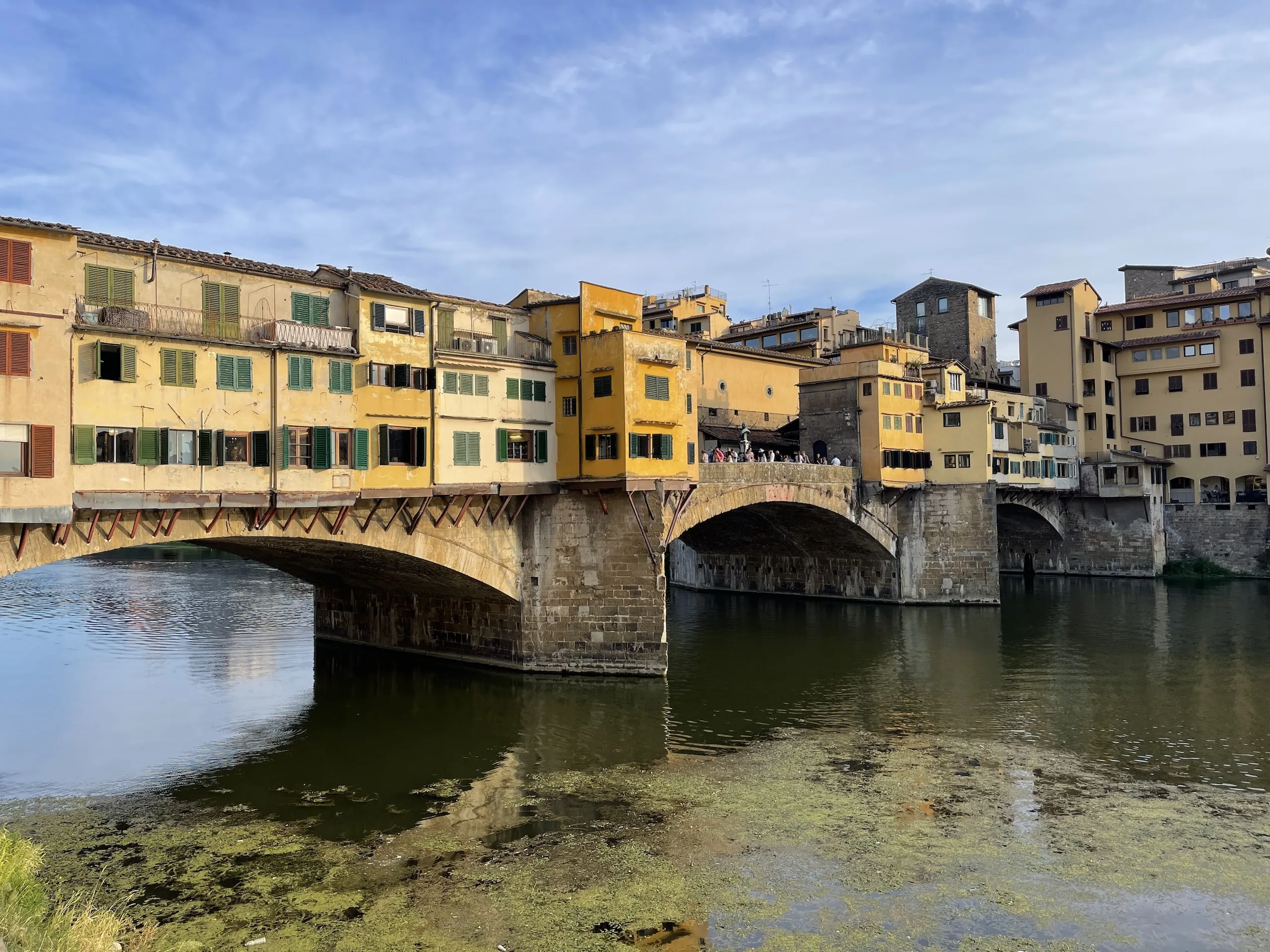 The mismatched shuttered shopfronts of the Ponte Vecchio seen from downstream
