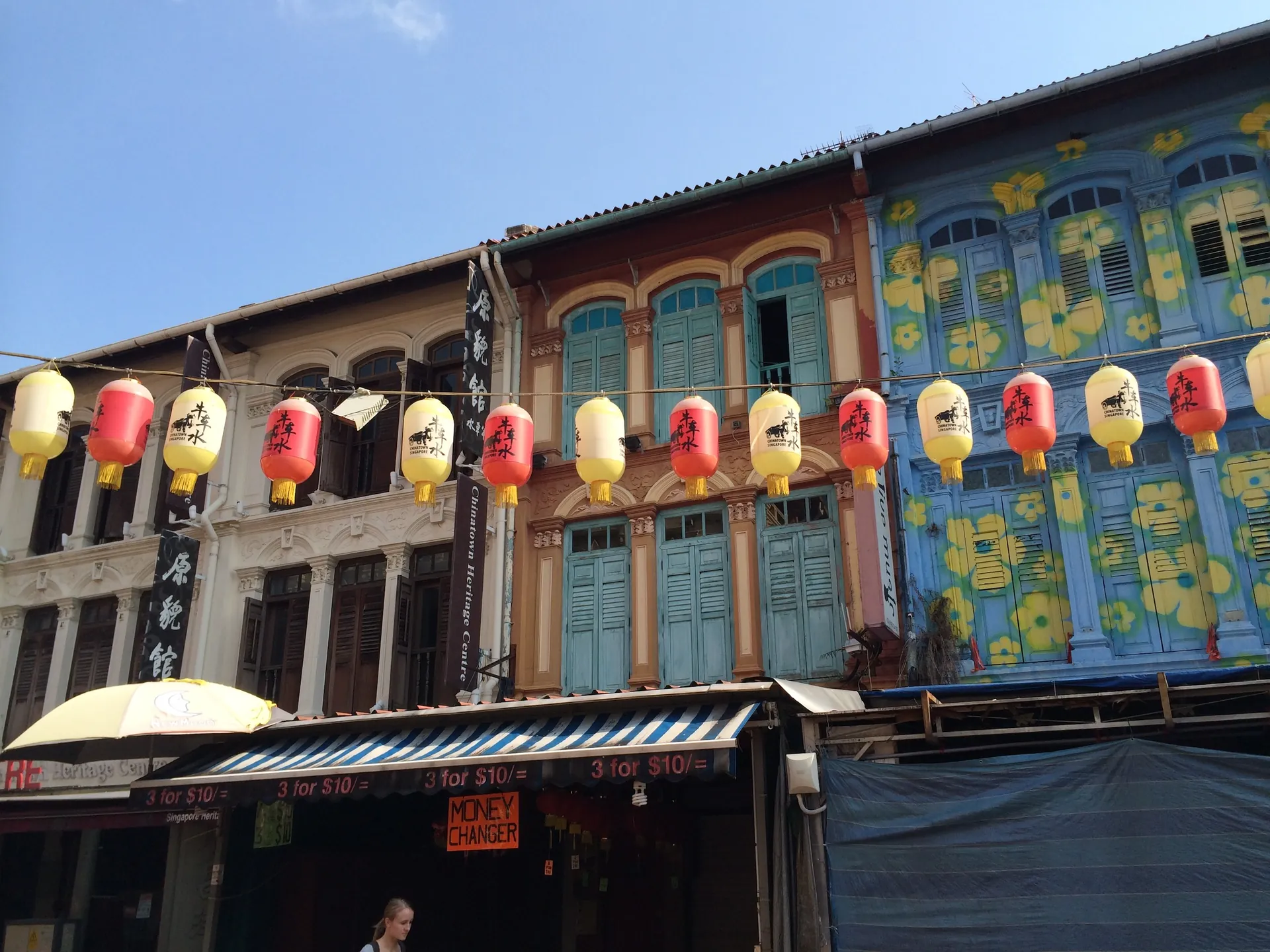 Restored shophouses in Chinatown with red and yellow lanterns strung across a blue facade