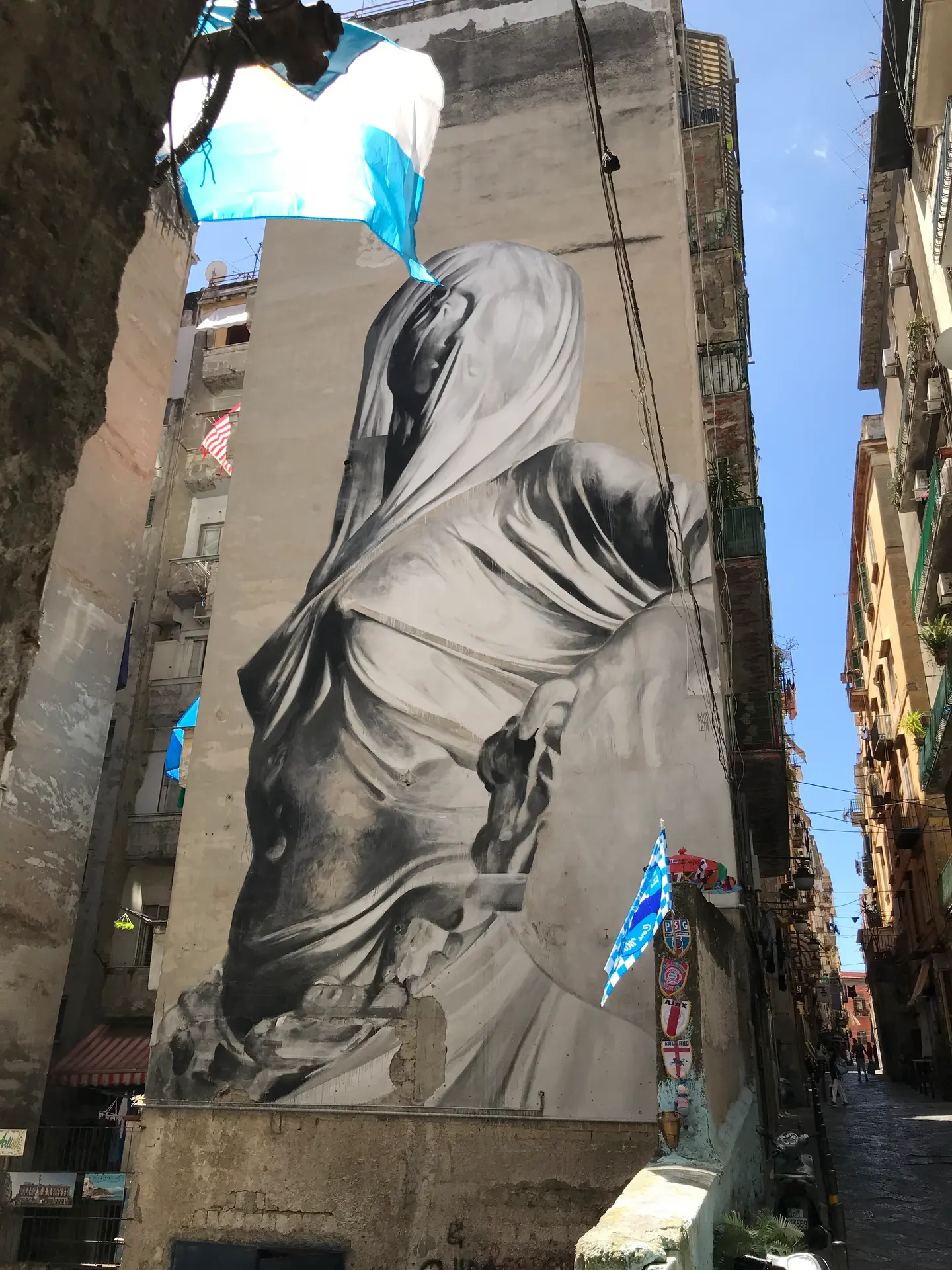 A tall grey mural of a draped figure on a building in the Spanish Quarter, Naples