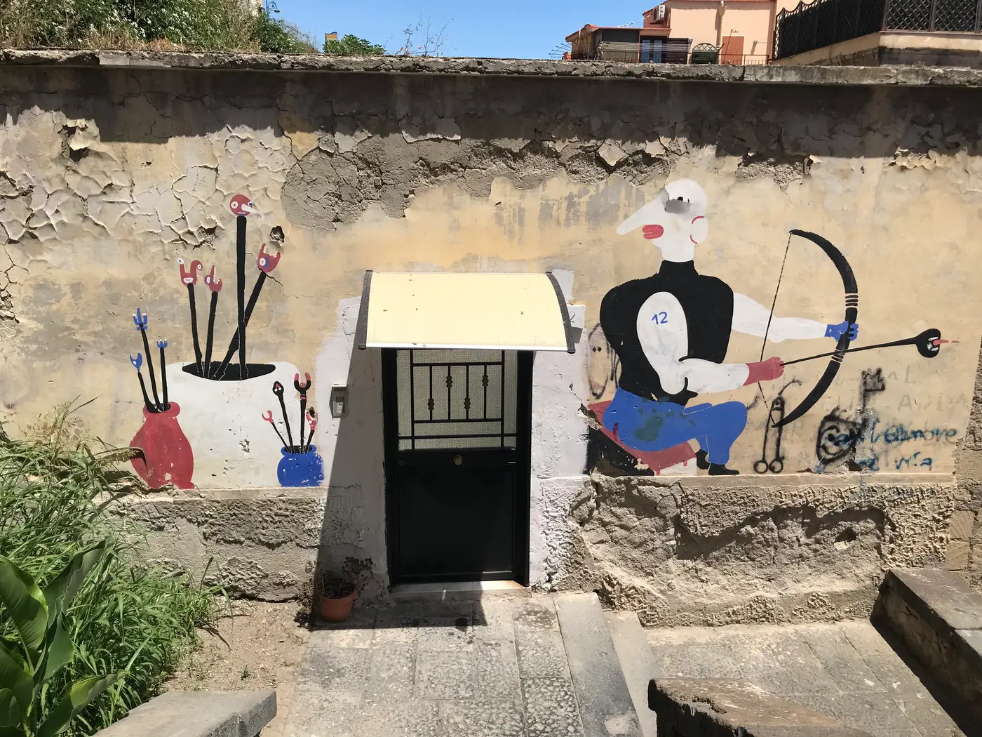 A mural of an archer and a pot of tools around a doorway in the Spanish Quarter, Naples