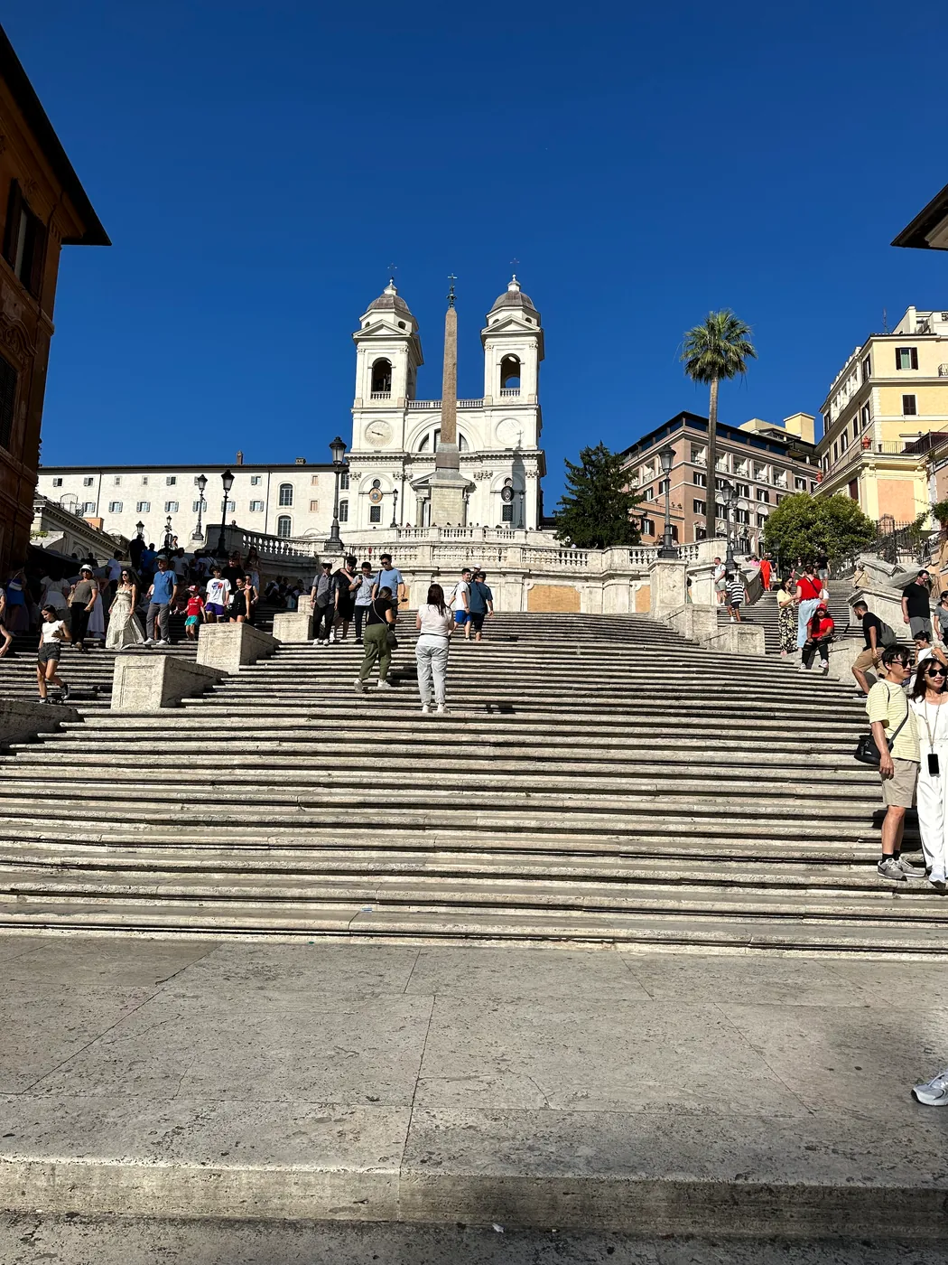 People climbing the sunlit Spanish Steps toward Trinità dei Monti.