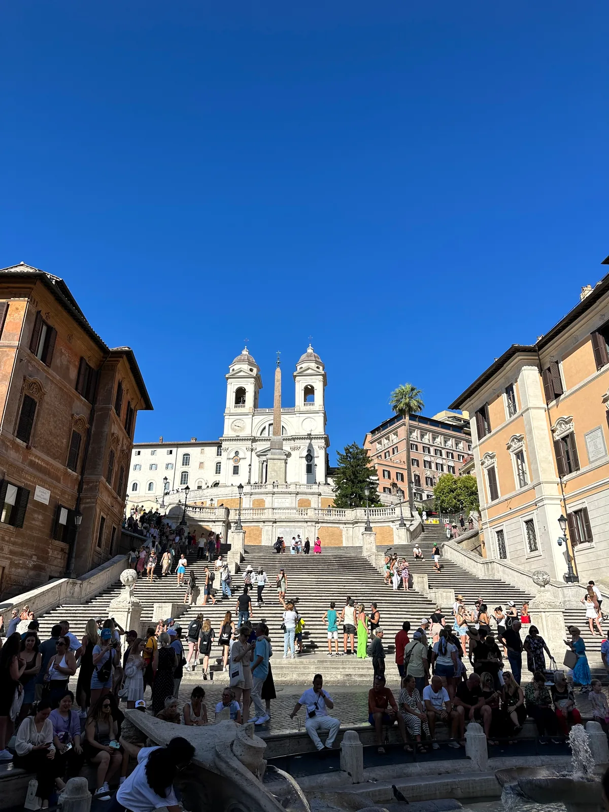 The Spanish Steps rising from Piazza di Spagna to Trinità dei Monti under blue sky.