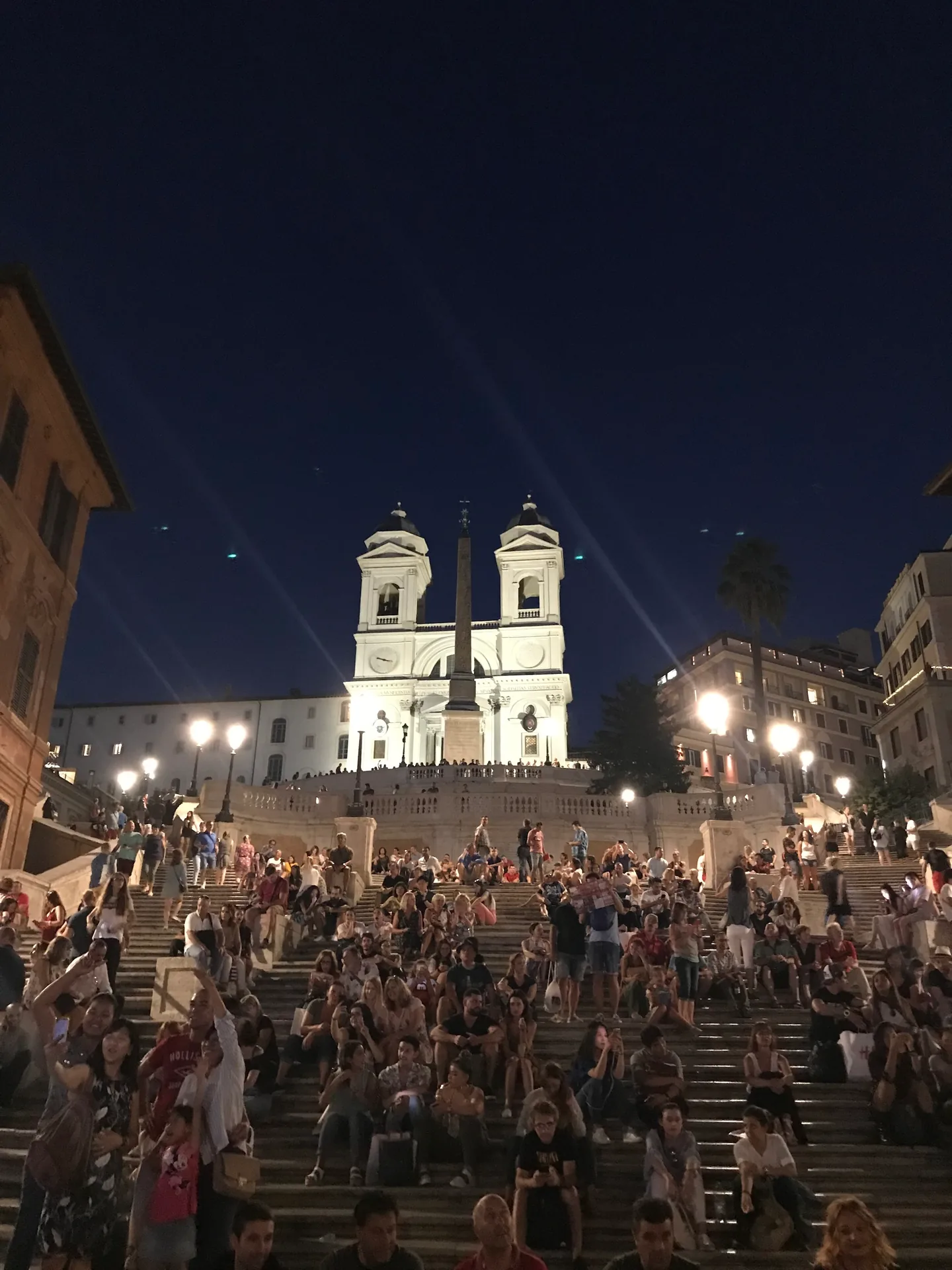The lit Trinità dei Monti up the crowded Spanish Steps at night.