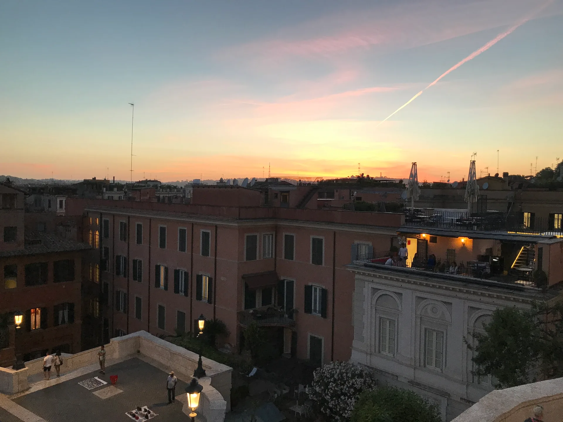 Pink sunset sky with a contrail over rooftops from the Spanish Steps.