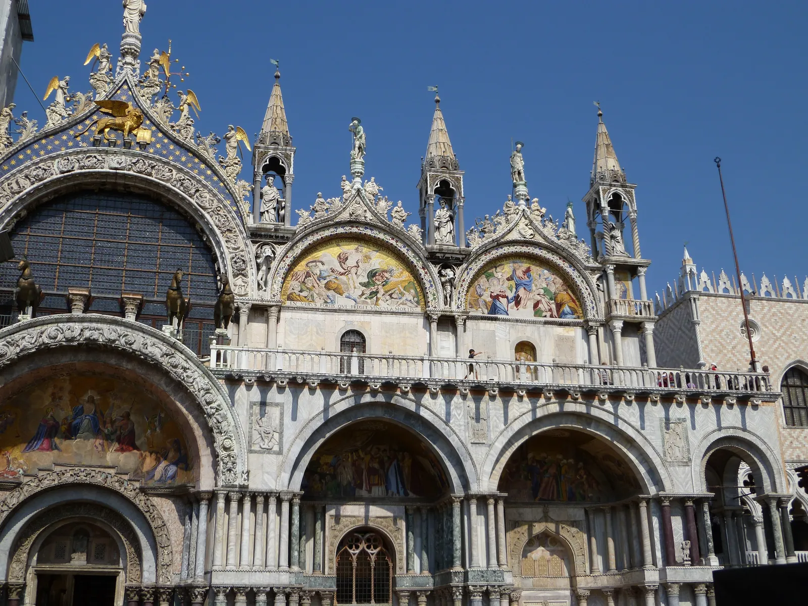 The full west facade of St Mark's Basilica in sunlight, with five portals, mosaics and a cluster of domes