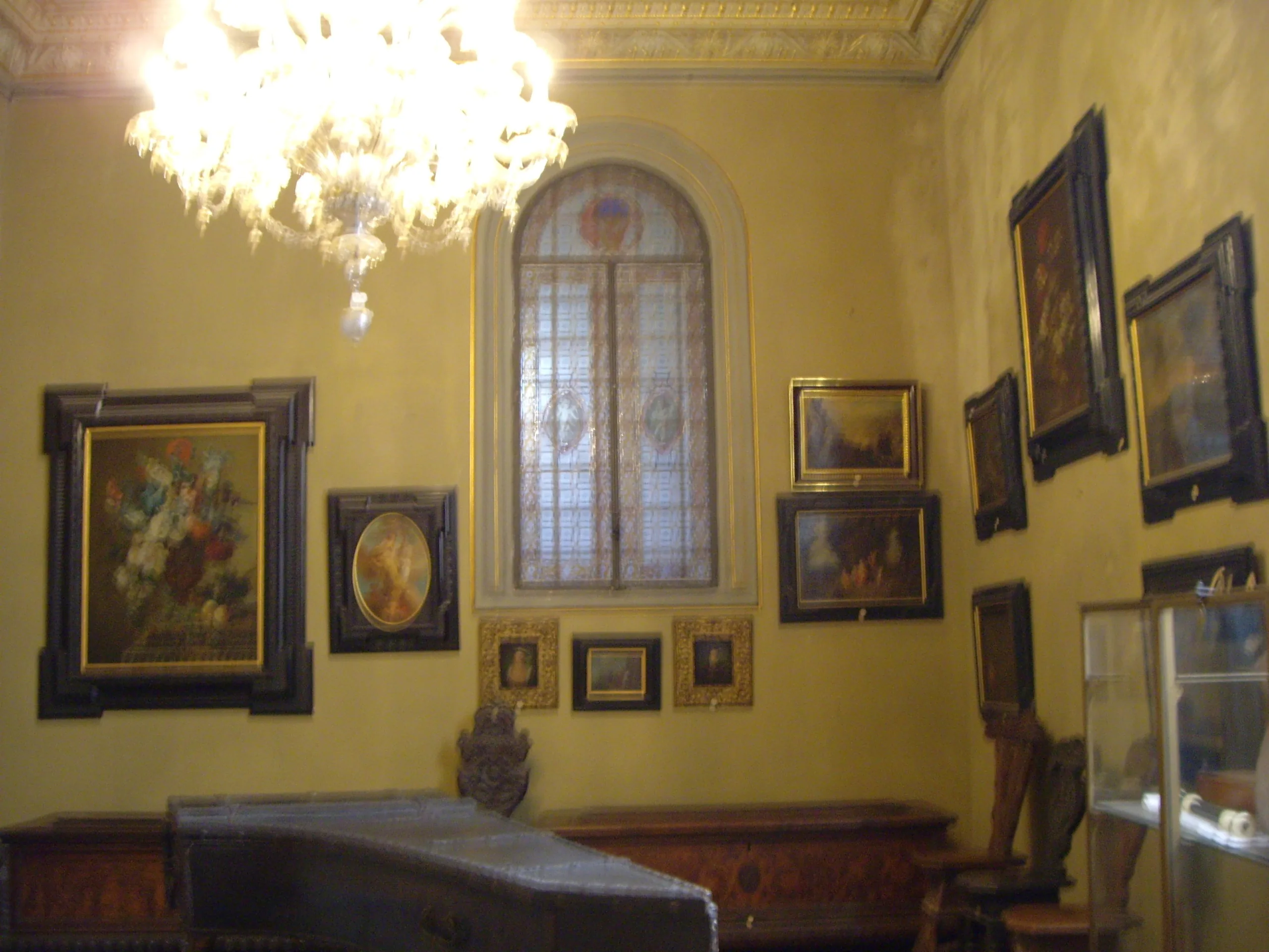 A Stibbert room hung floor to ceiling with paintings under a glass chandelier