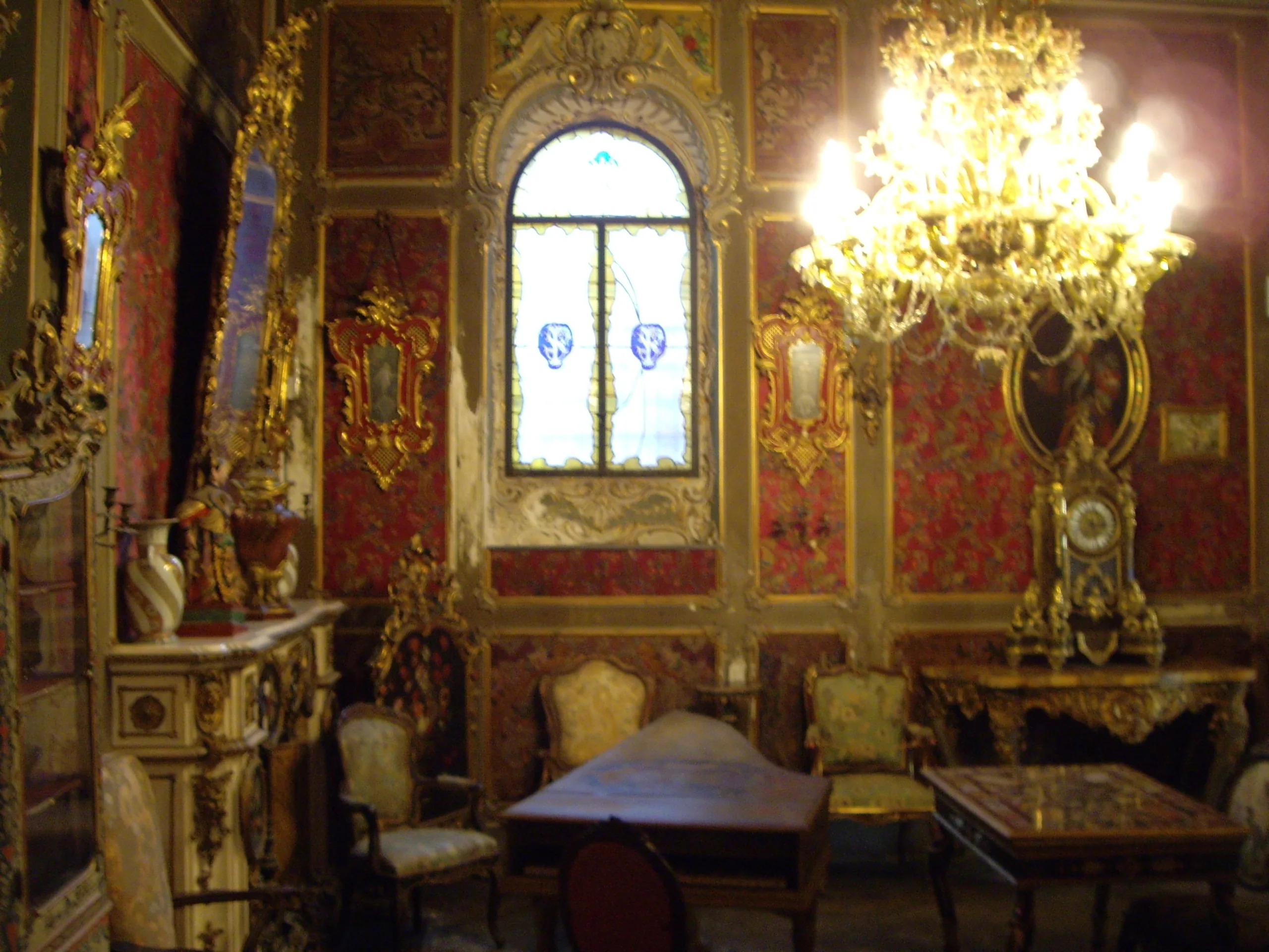 A crimson and gilt reception room in the Villa Stibbert, with chandelier and stained glass