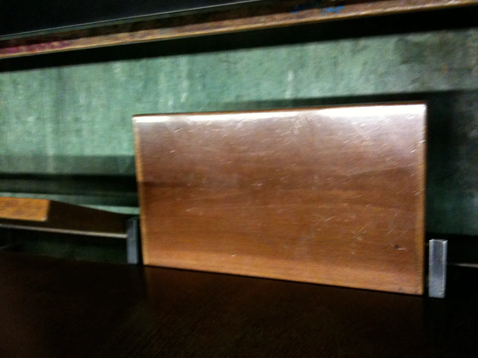 A hinged wooden writing desk folded up against a green wall in a lecture hall.
