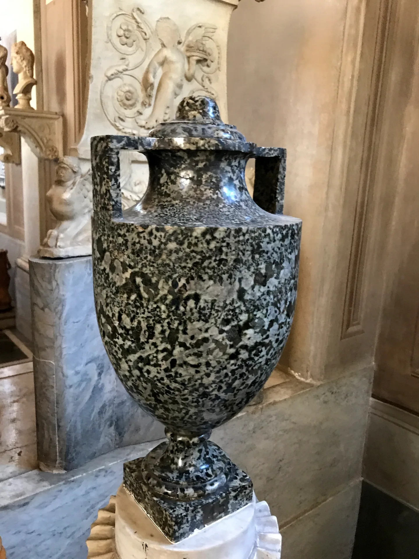 Large ancient urn carved from dark speckled stone on a marble base.