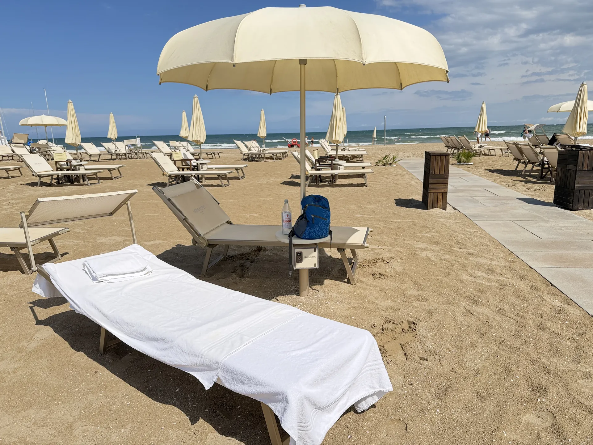 A dressed lounger under a parasol with rows of closed parasols and the sea behind