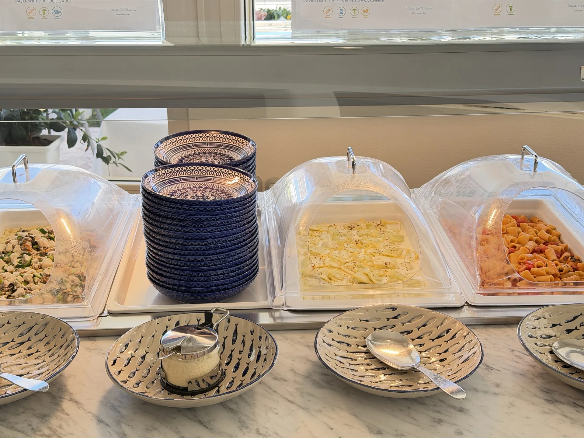 Trays of ravioli and maccheroni under covers on the beach buffet counter