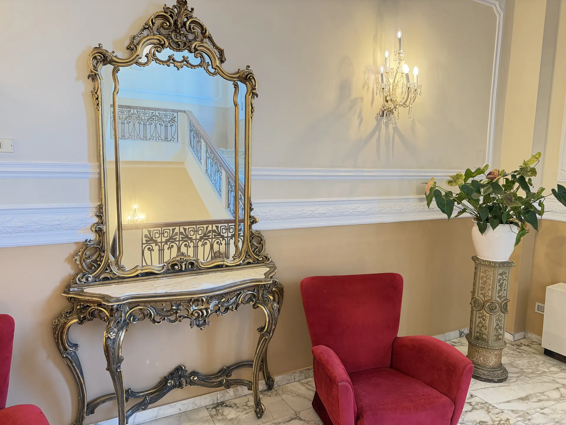 Gilt console and carved mirror with a crimson armchair on the hotel's marble floor