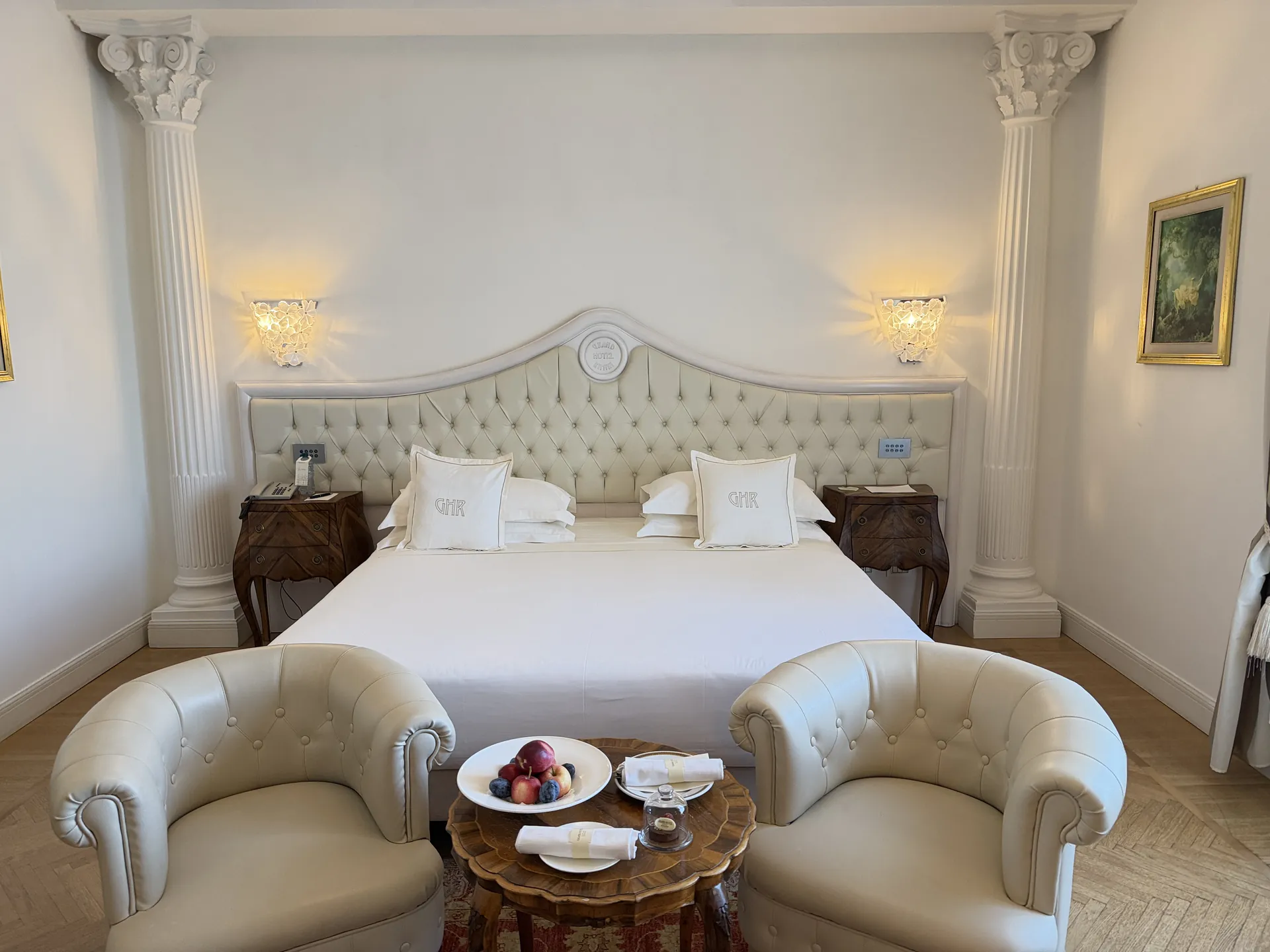 Hotel room with fluted pilasters, a red patterned rug and armchairs at a marquetry table