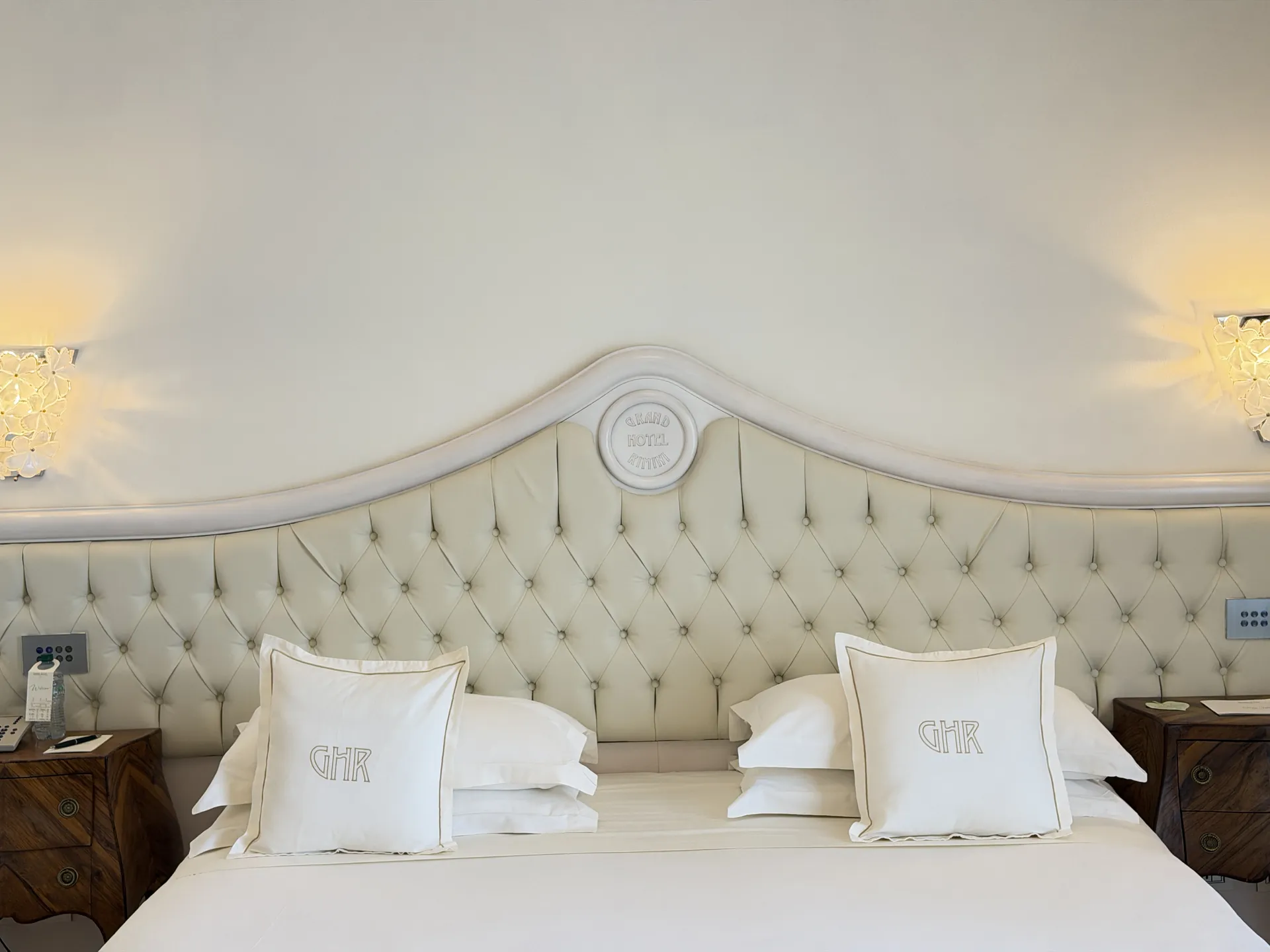 Tufted headboard with the hotel monogram on the pillows and Murano glass sconces