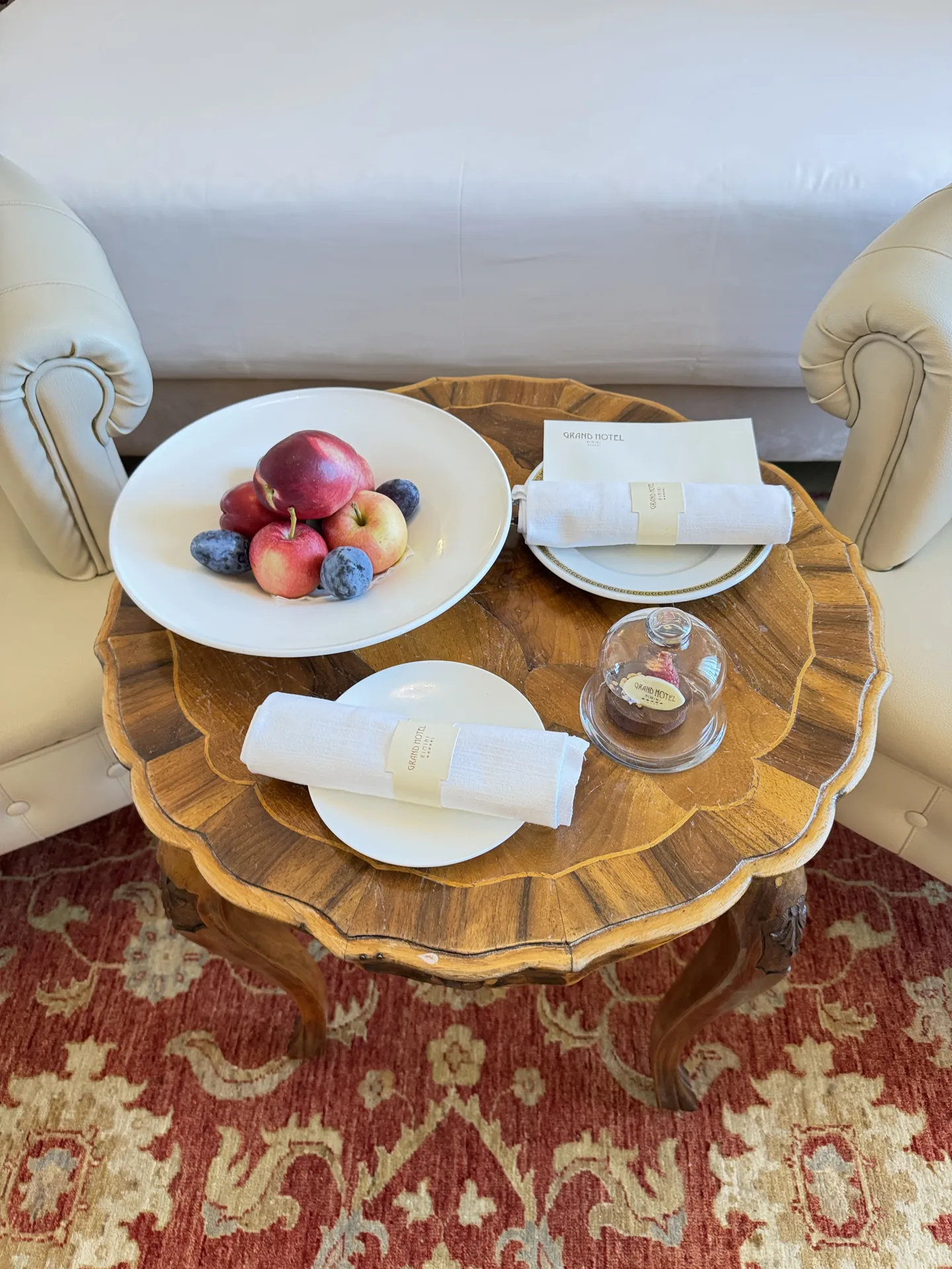 Welcome fruit and a chocolate under a glass cloche on an inlaid table in a hotel room
