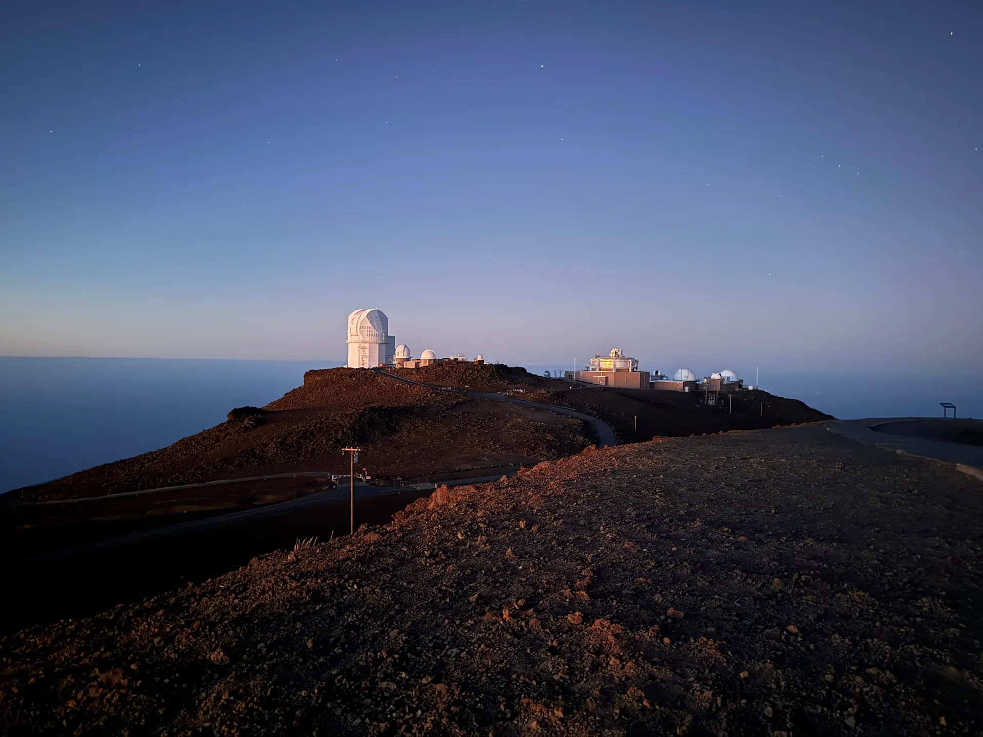 White observatory domes on a red cinder ridge under a dawn sky