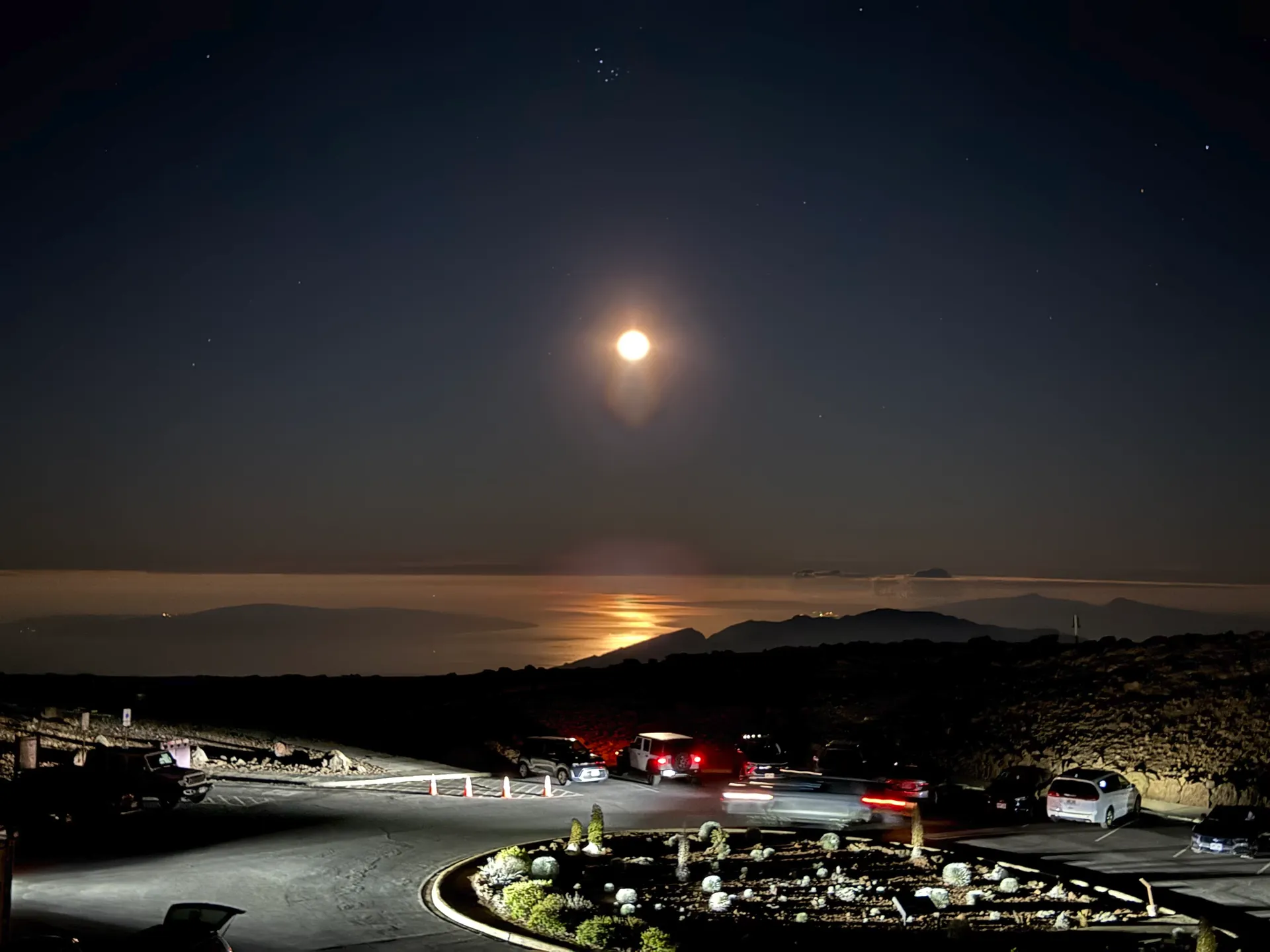 Cars parked at the Haleakala summit before dawn under a bright moon over the ocean