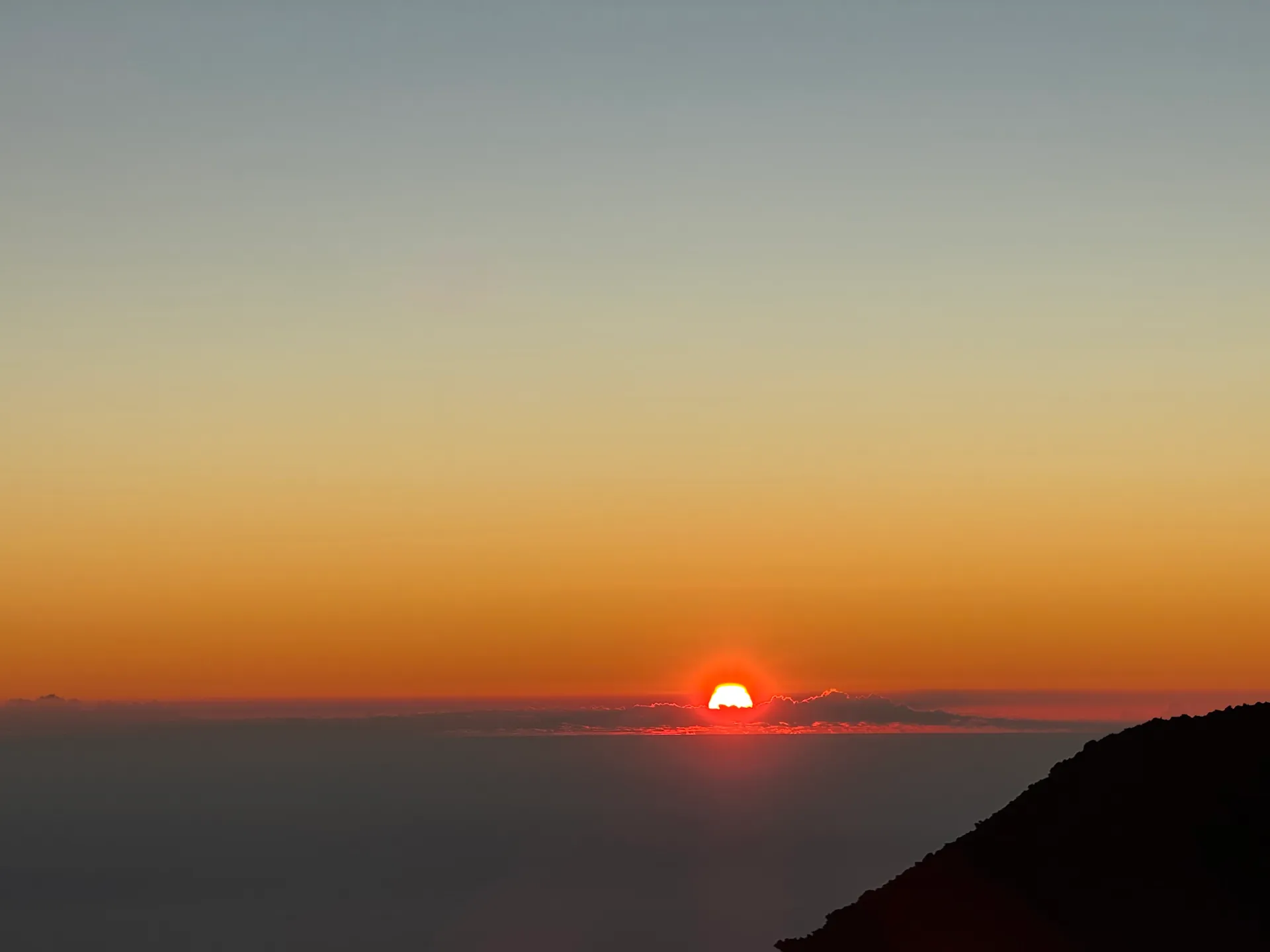 Orange sun disc resting on a cloud deck seen from above