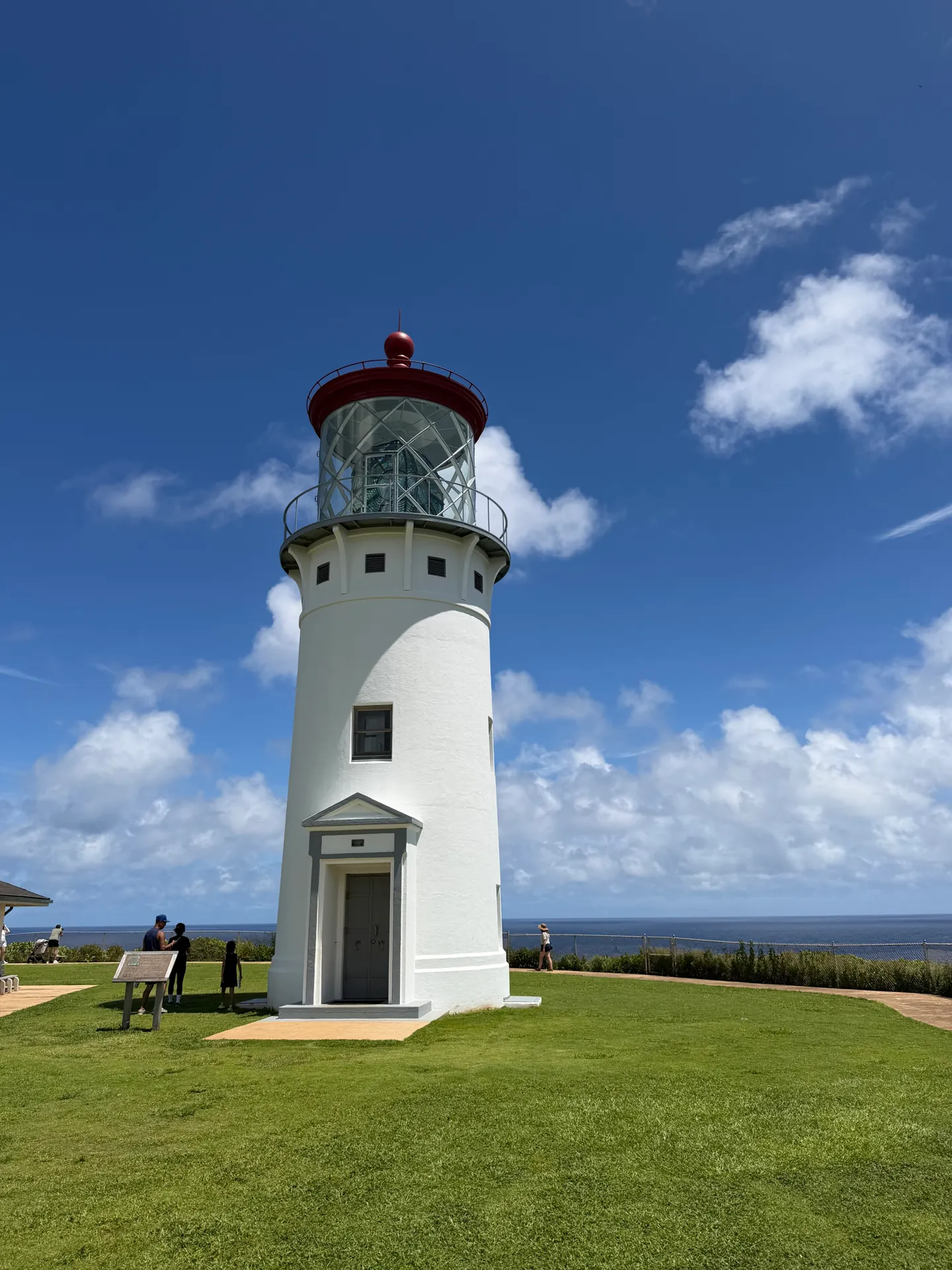 The white Kilauea Lighthouse with a red top on a green point under a blue sky