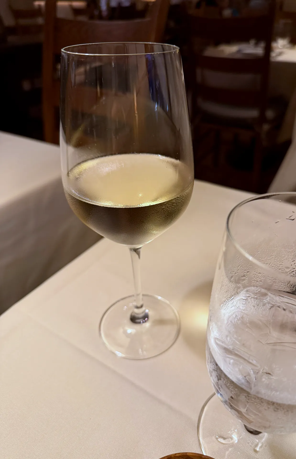 A glass of Assyrtiko white wine on a white tablecloth with the dining room behind.